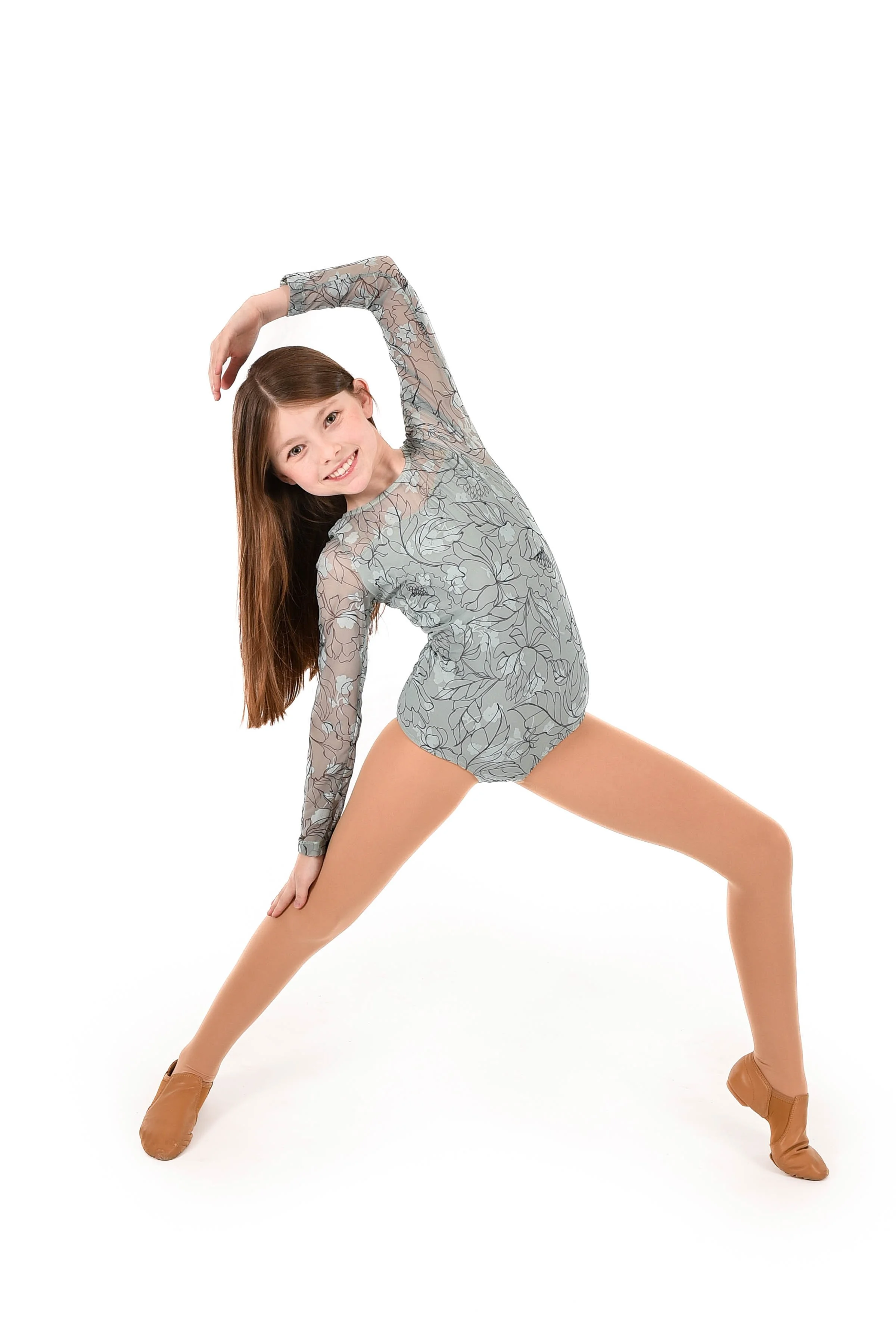 Young girl in a floral dance costume poses in a wide stance, smiling with one arm overhead and the other touching her leg, performing a ballet pose.