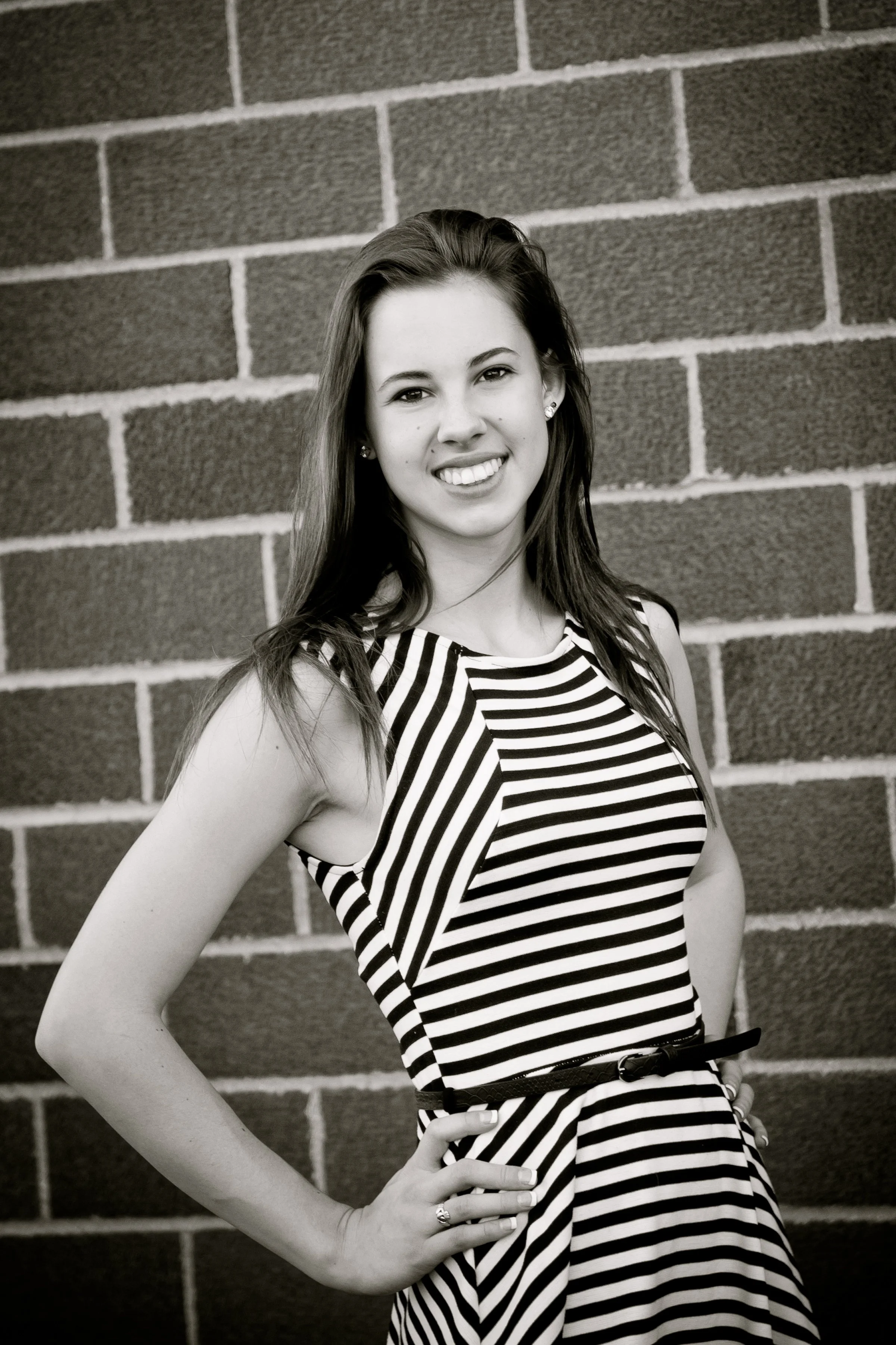 Black and white photo of a young woman in a striped dress standing against a brick wall with a confident smile.