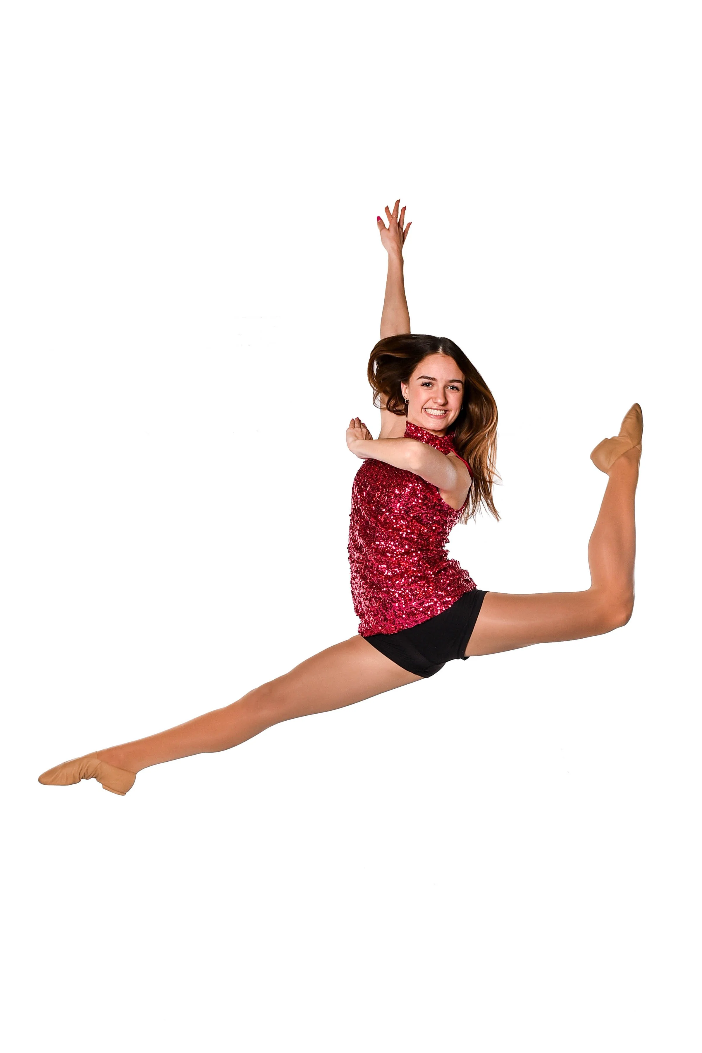A young woman in a glittery red top and black shorts performing a dance leap with a big smile, against a plain white background.