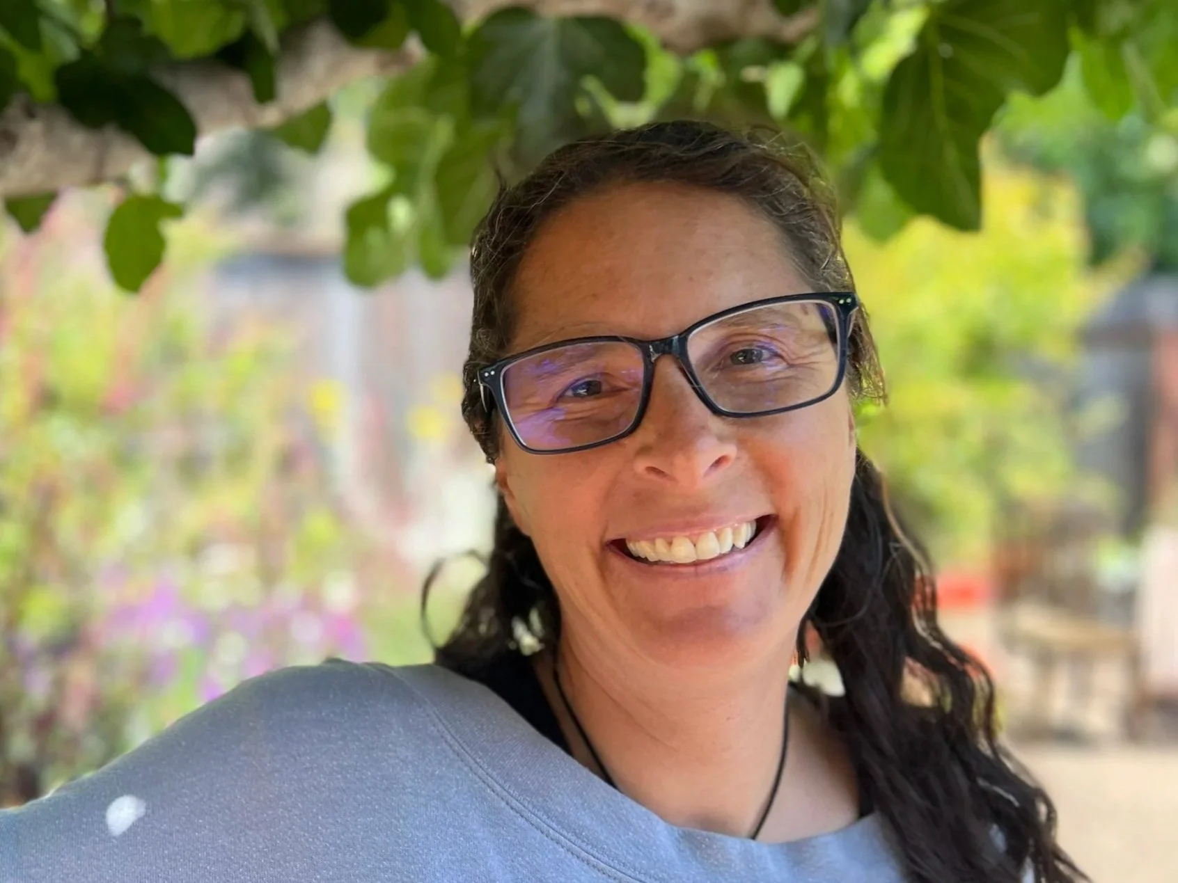 Smiling woman wearing glasses, in front of green leaves and a blurred green background. 