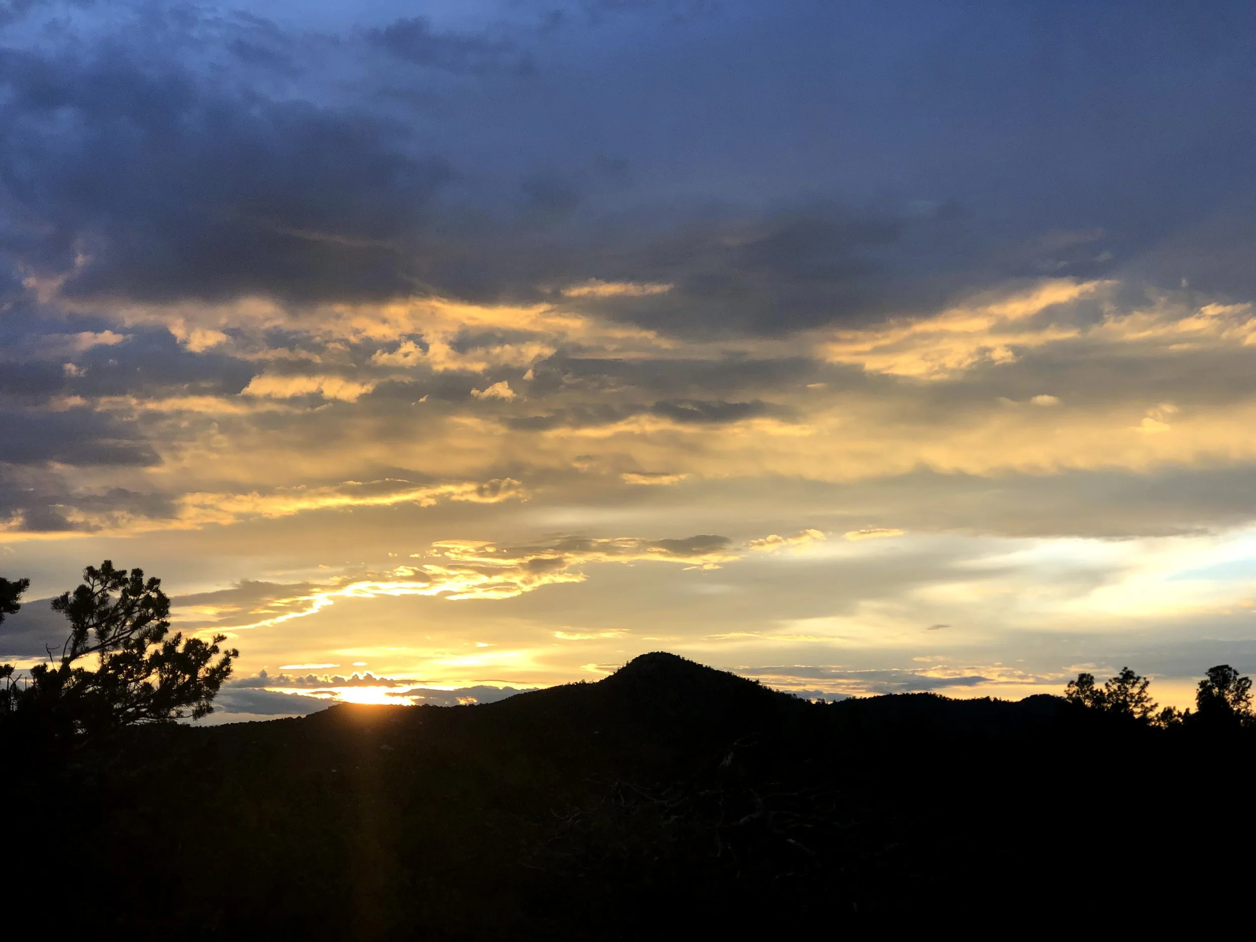 Sunset over silhouetted hills with partly cloudy sky and golden light.