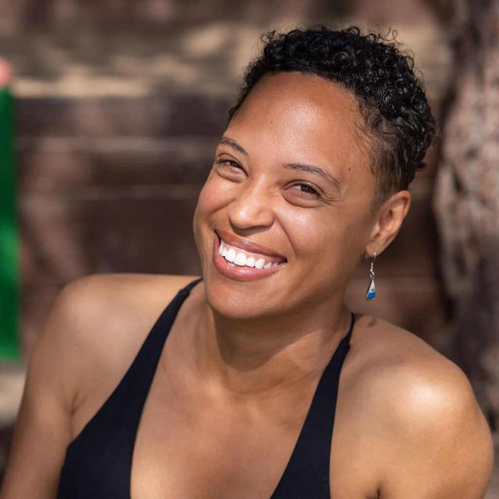 Smiling woman wearing a black tank top in front of a brick wall. 