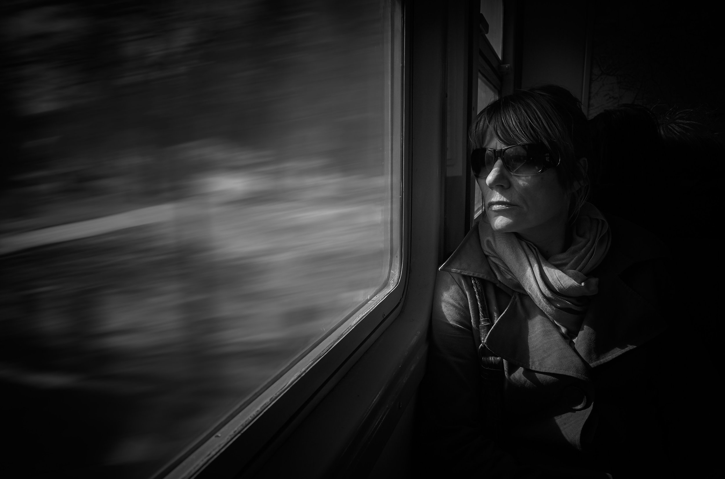 Black and white photo of a woman on a train looking out the window.