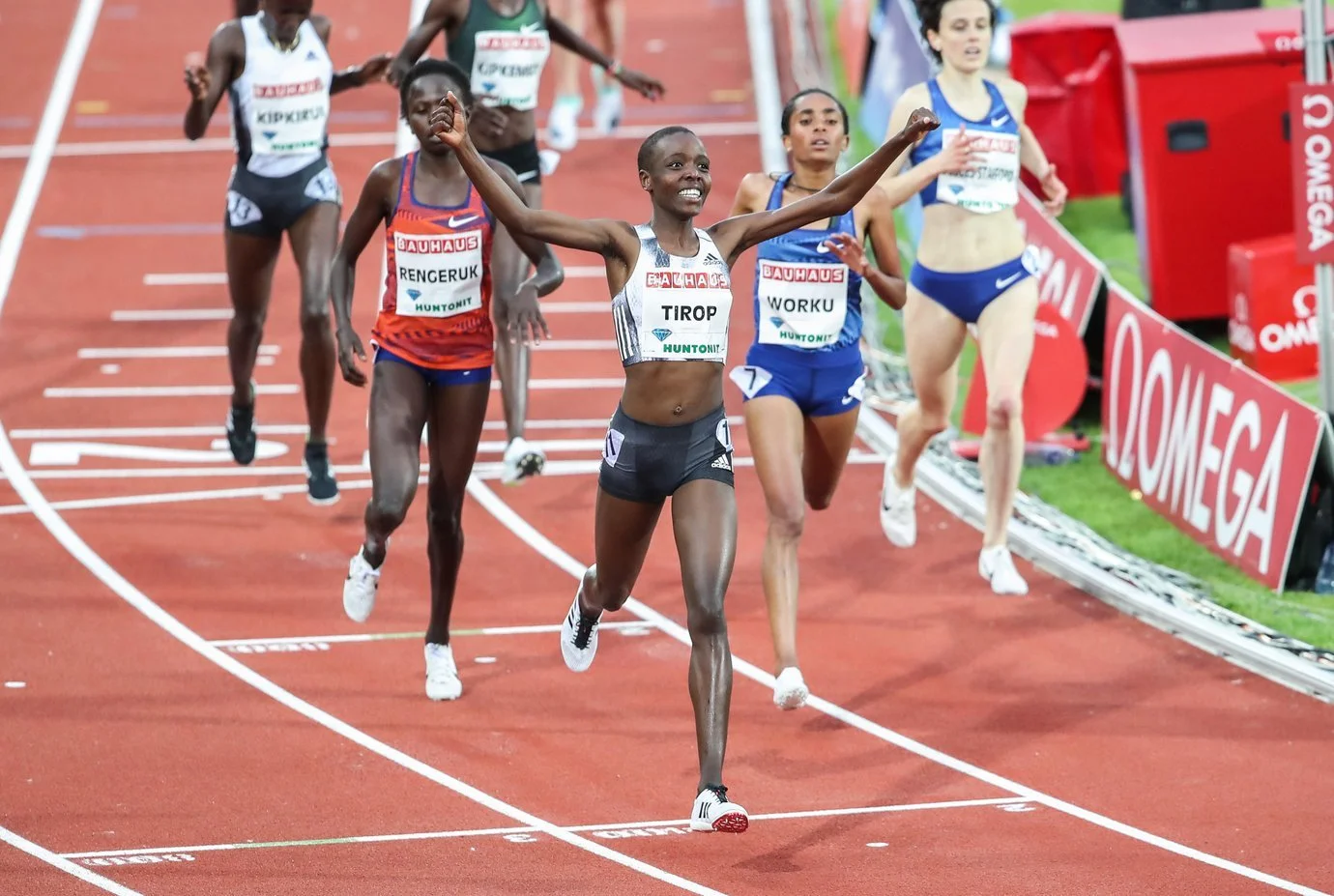 A running track with six runners. Agnes Tirop is in the front with her arms raised in victory.