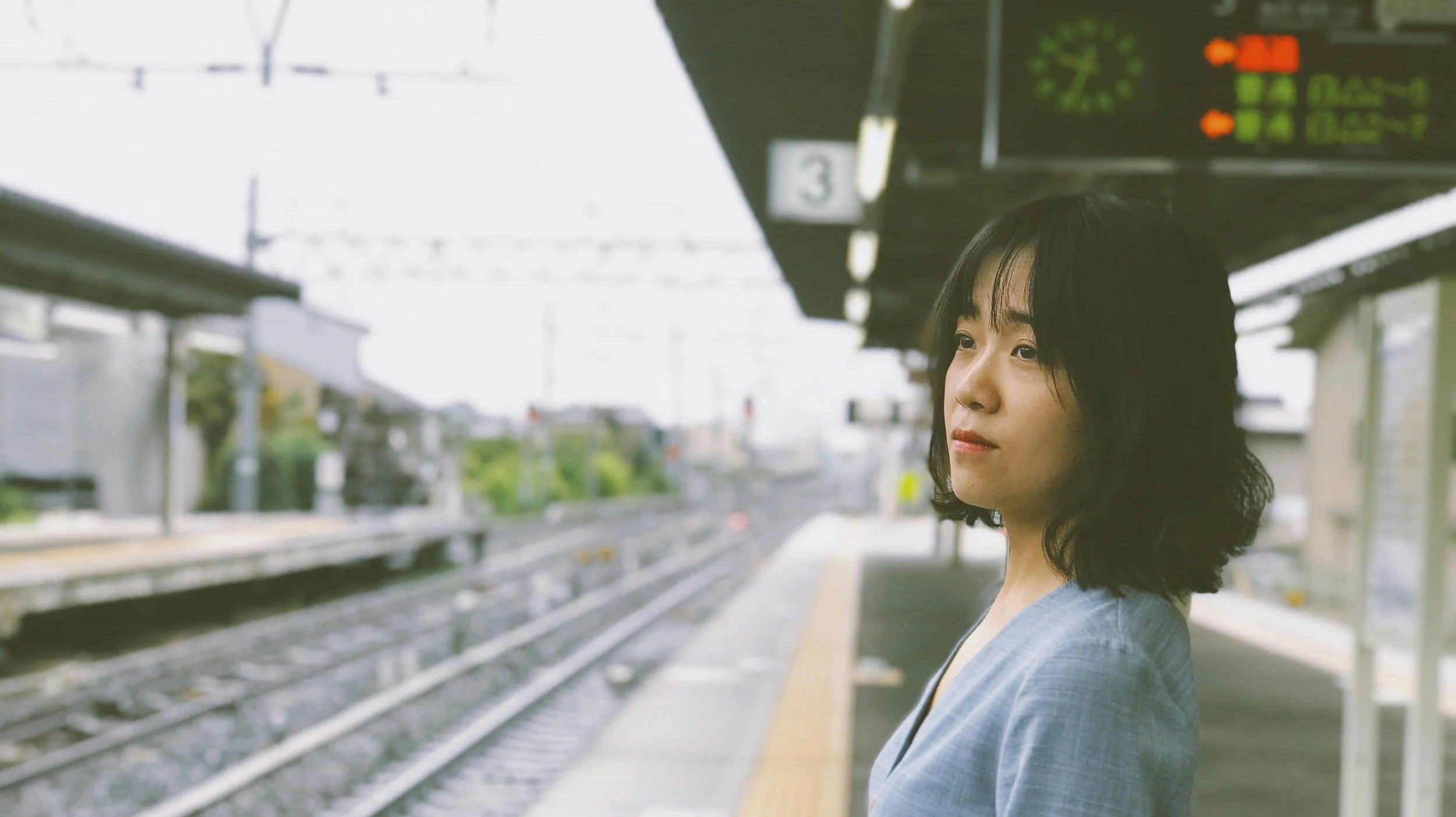 A Japanese woman waiting for a train and staring into the distance.