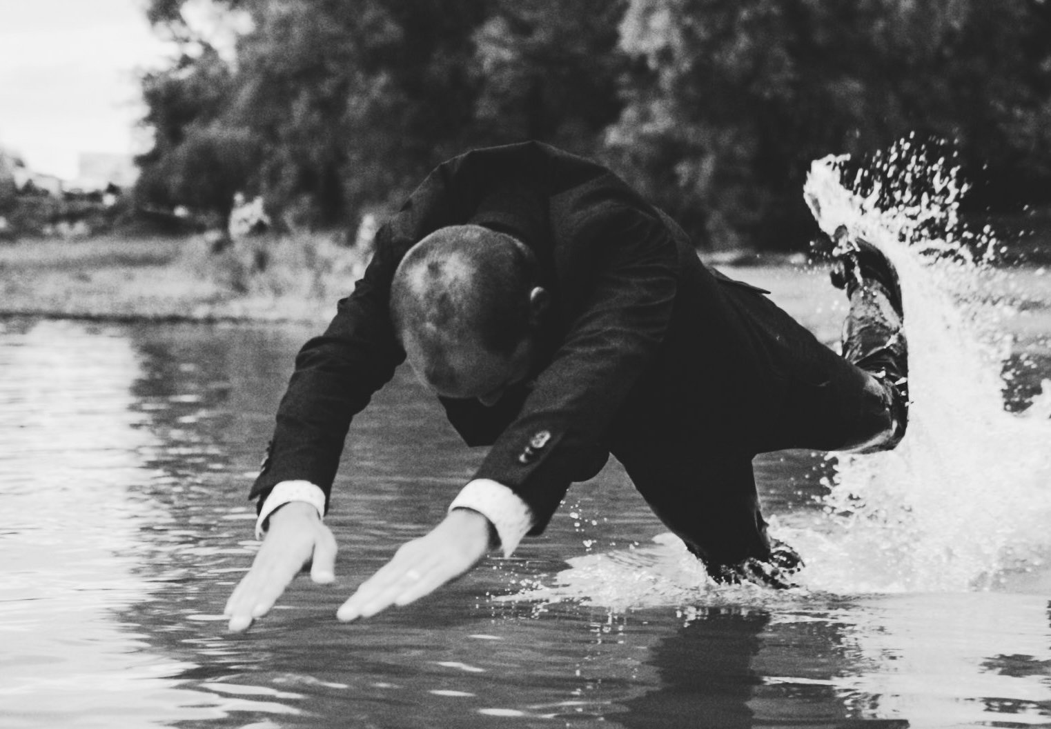 Black and white photo of a man dressed in a suit diving into a stream.