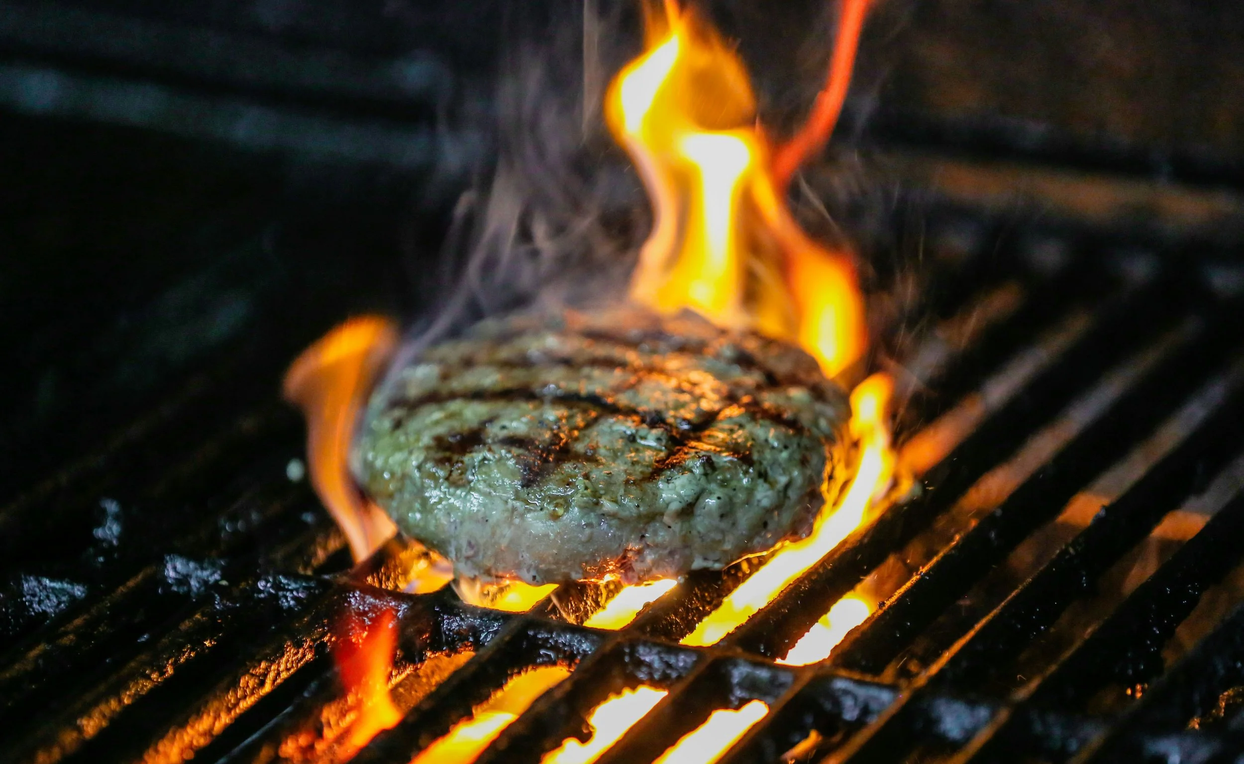 A hamburger cooking a grill surrounded by flames.
