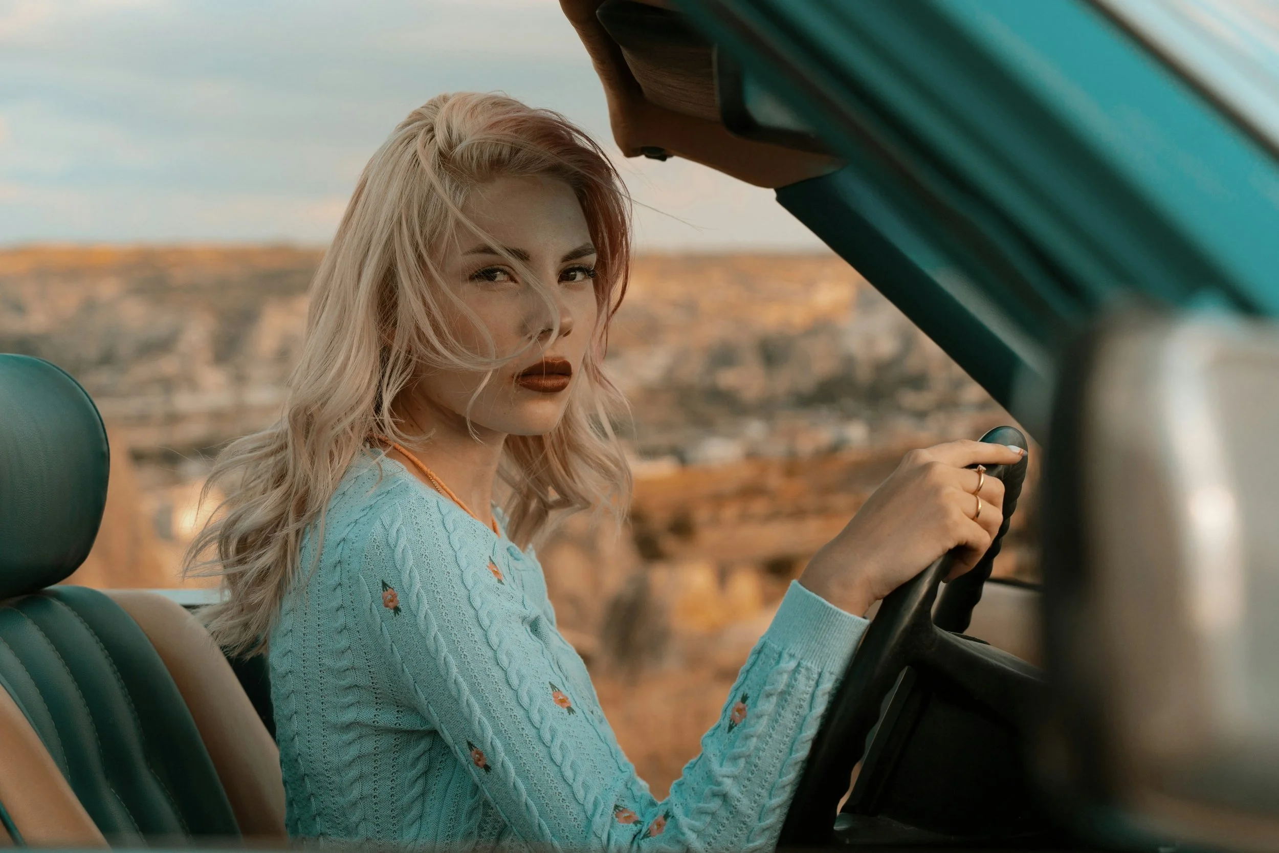 A pretty blonde woman driving a convertible in the desert. She has a judgmental look on her face.