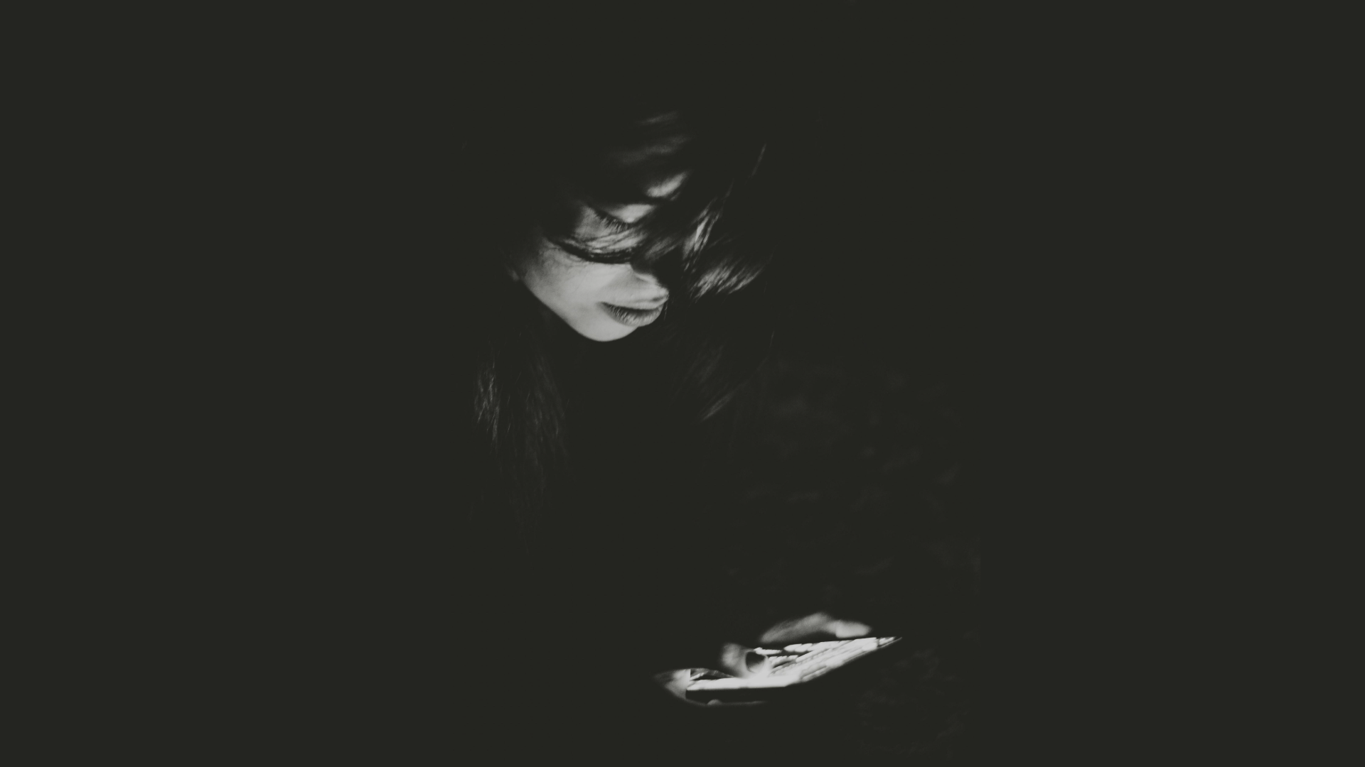 Black and white photo of a woman looking at her cell phone in the dark.