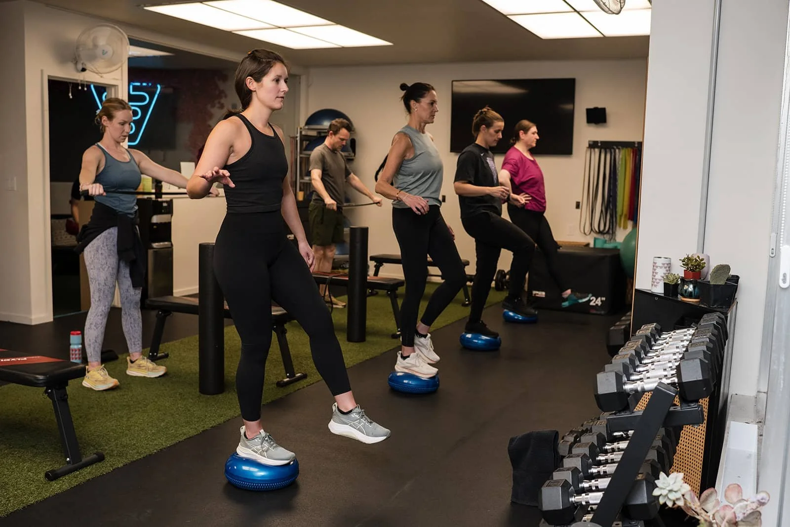 Group of women participating in a fitness class, standing on balance balls, in a gym setting.