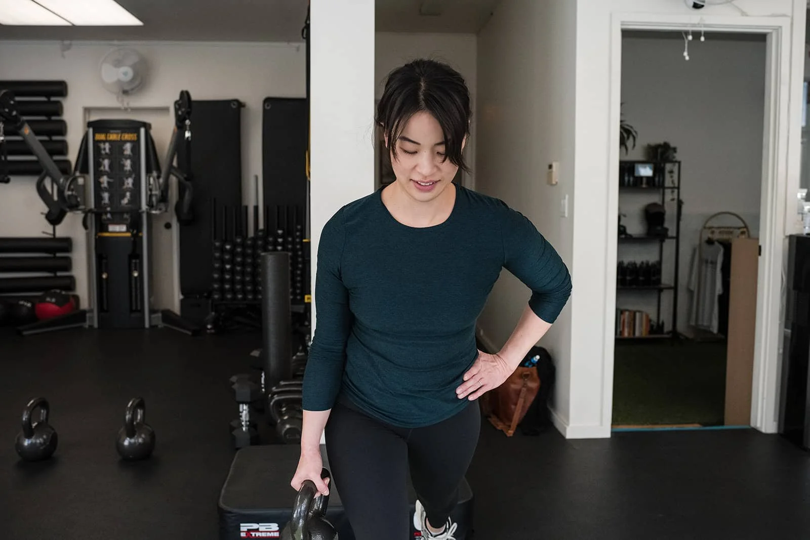 Woman in workout attire performing a step-up exercise with kettlebells in a home gym.