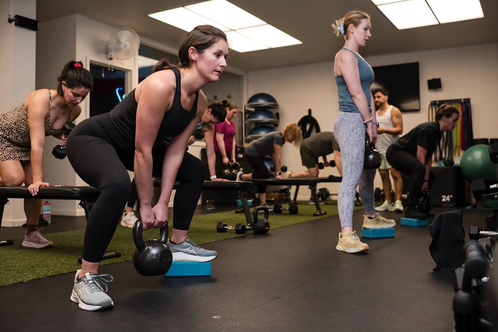 People participating in a group workout class in a gym, performing kettlebell exercises during a fitness session.