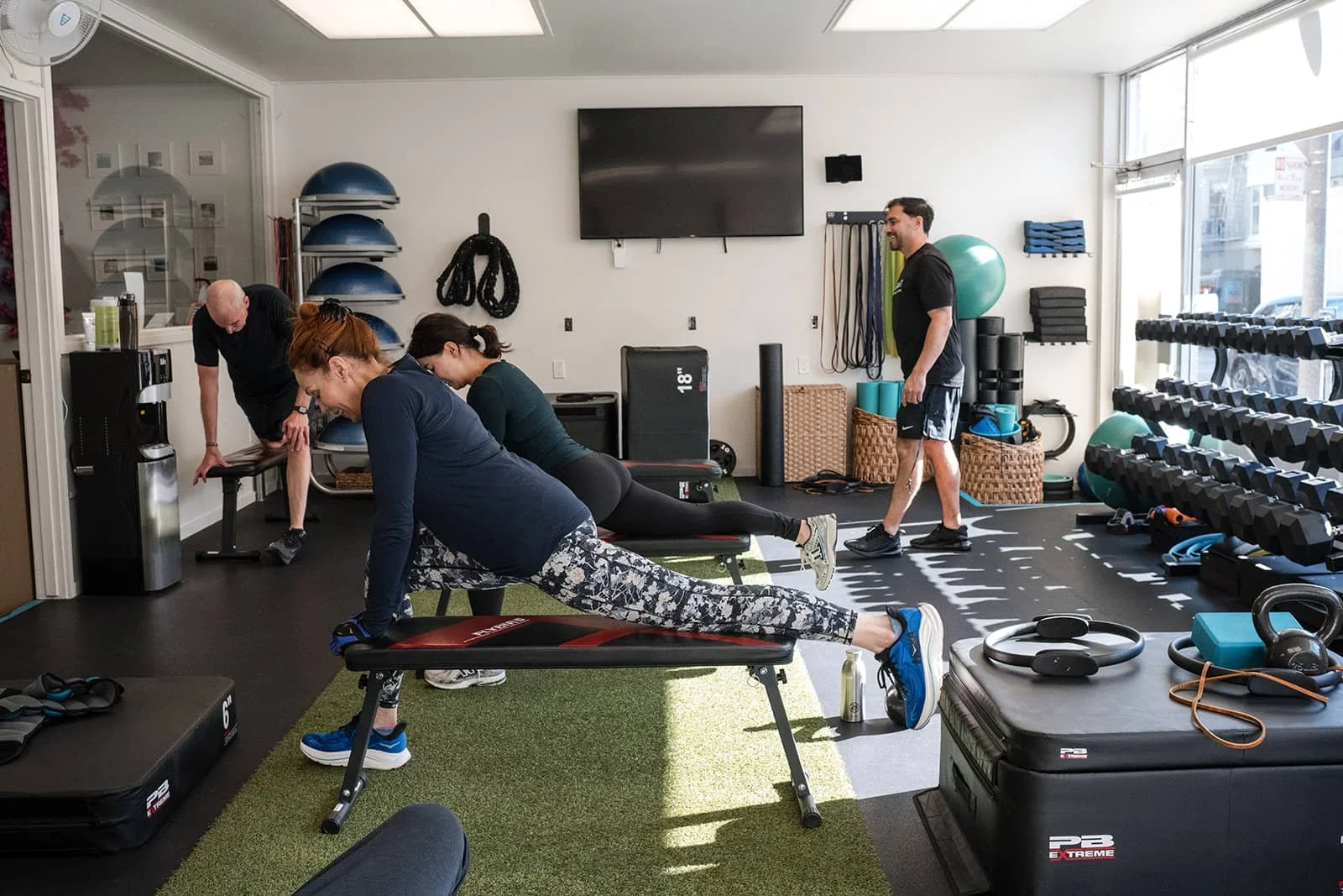 People working out in a fitness studio, with weights, exercise balls, and workout equipment visible.