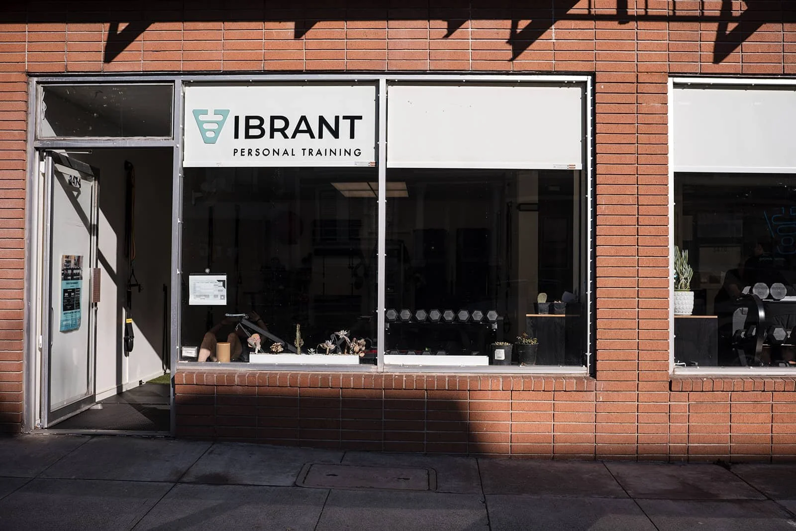 Exterior view of a brick building with large windows and a sign reading 'VIBRANT PERSONAL TRAINING' on the storefront.