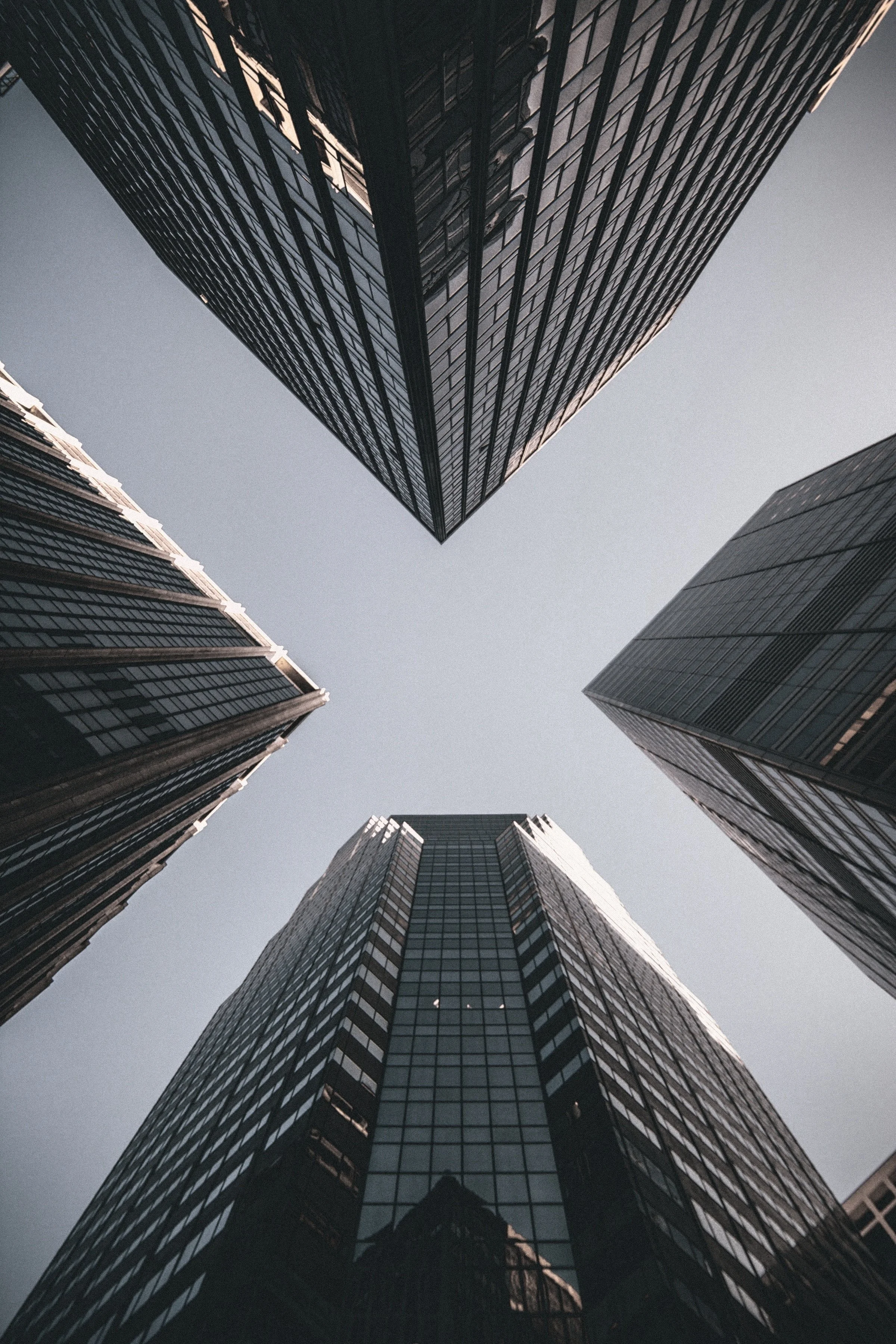 Upward view of four tall modern glass skyscrapers converging towards the sky.