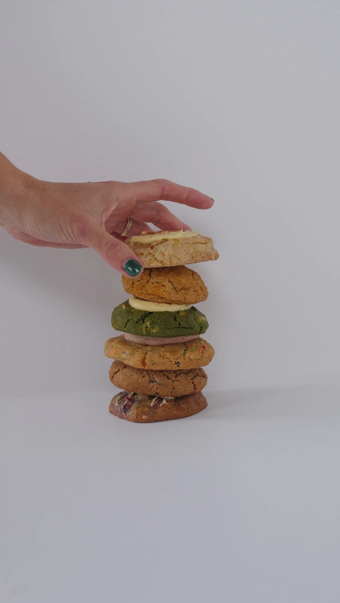 A hand stacking various decorated cookies on a plain white background.