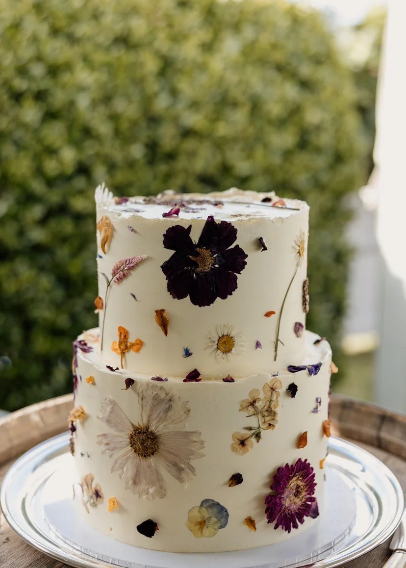 A two-tiered white cake decorated with pressed edible flowers.