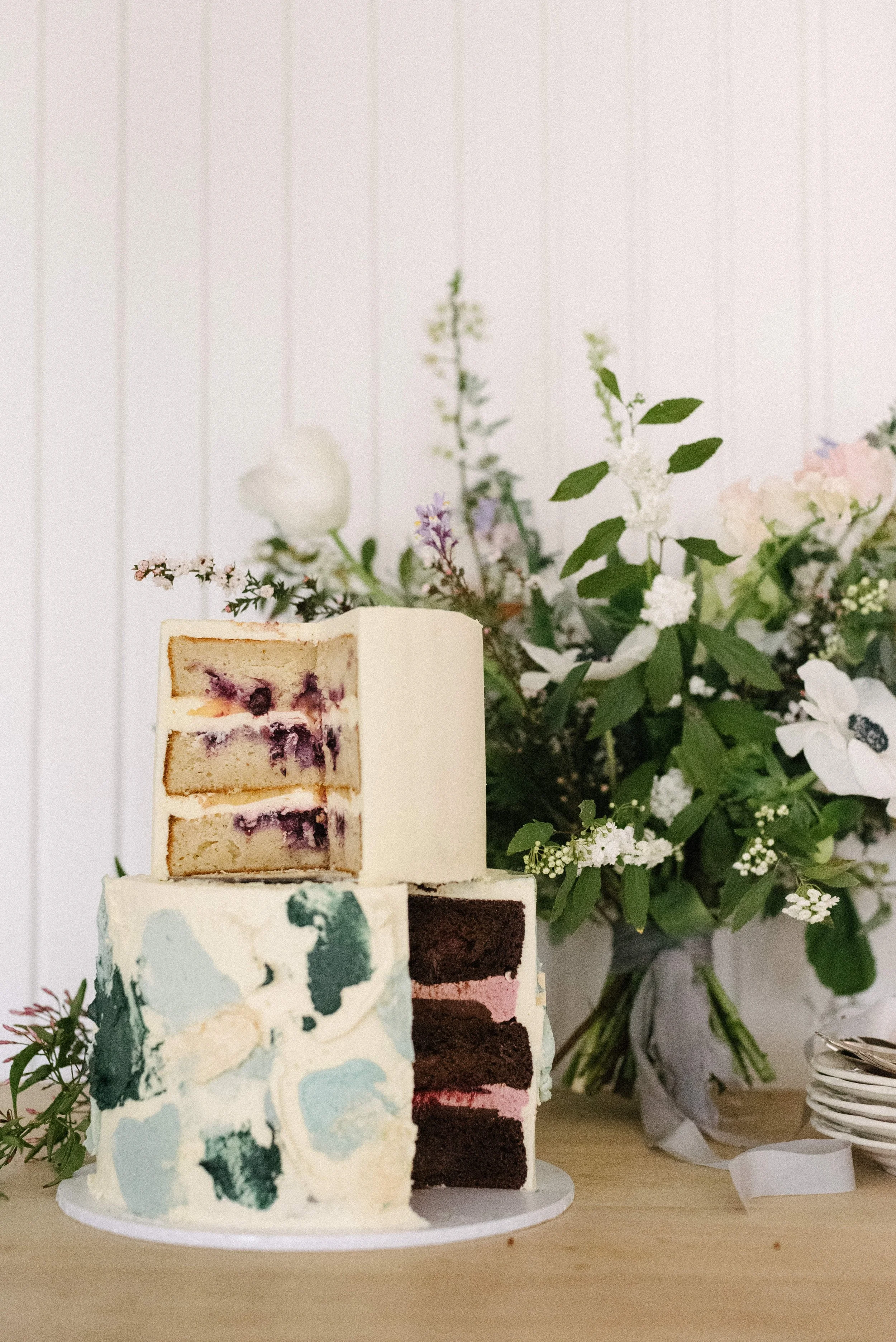 Two layered cakes on a table with a bouquet of flowers in the background