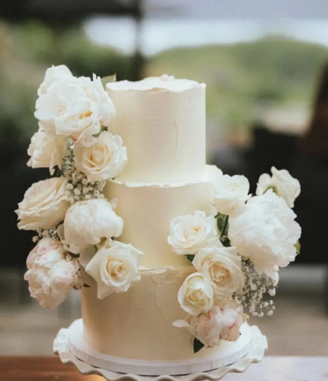 Two-tiered white wedding cake decorated with white roses and small white flowers.