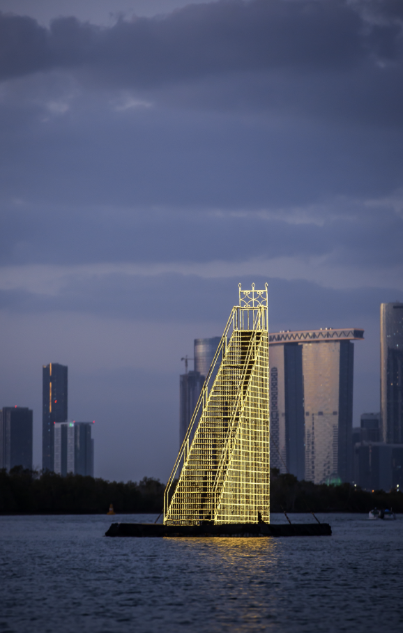 Illuminated yellow steel structure floating on water with city skyline and dark cloudy sky in the background. Dawaran, 2022. Ayesha Hadhir, Rawdha Al Ketbi and Shaikha Al Ketbi.