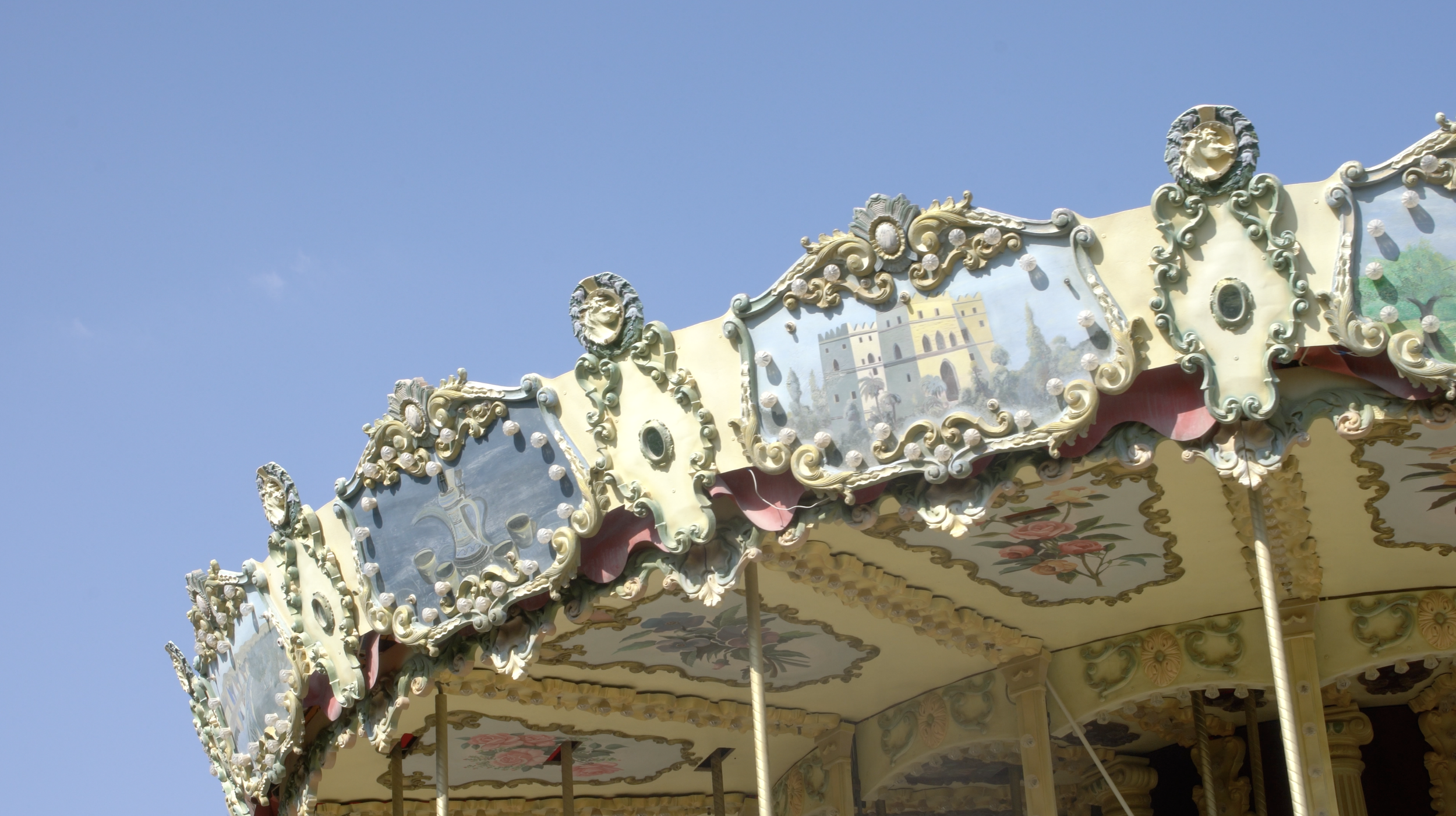 Close-up of an ornate vintage carousel with decorative painted panels and golden embellishments against a clear blue sky.