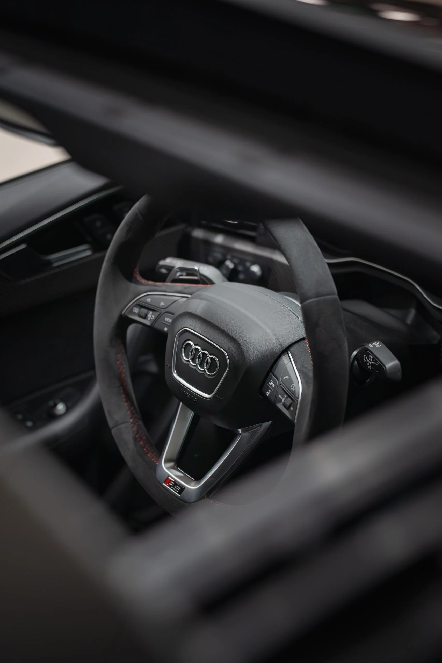Interior of an Audi car, showing the steering wheel with the Audi logo, multifunction buttons, and a digital display.