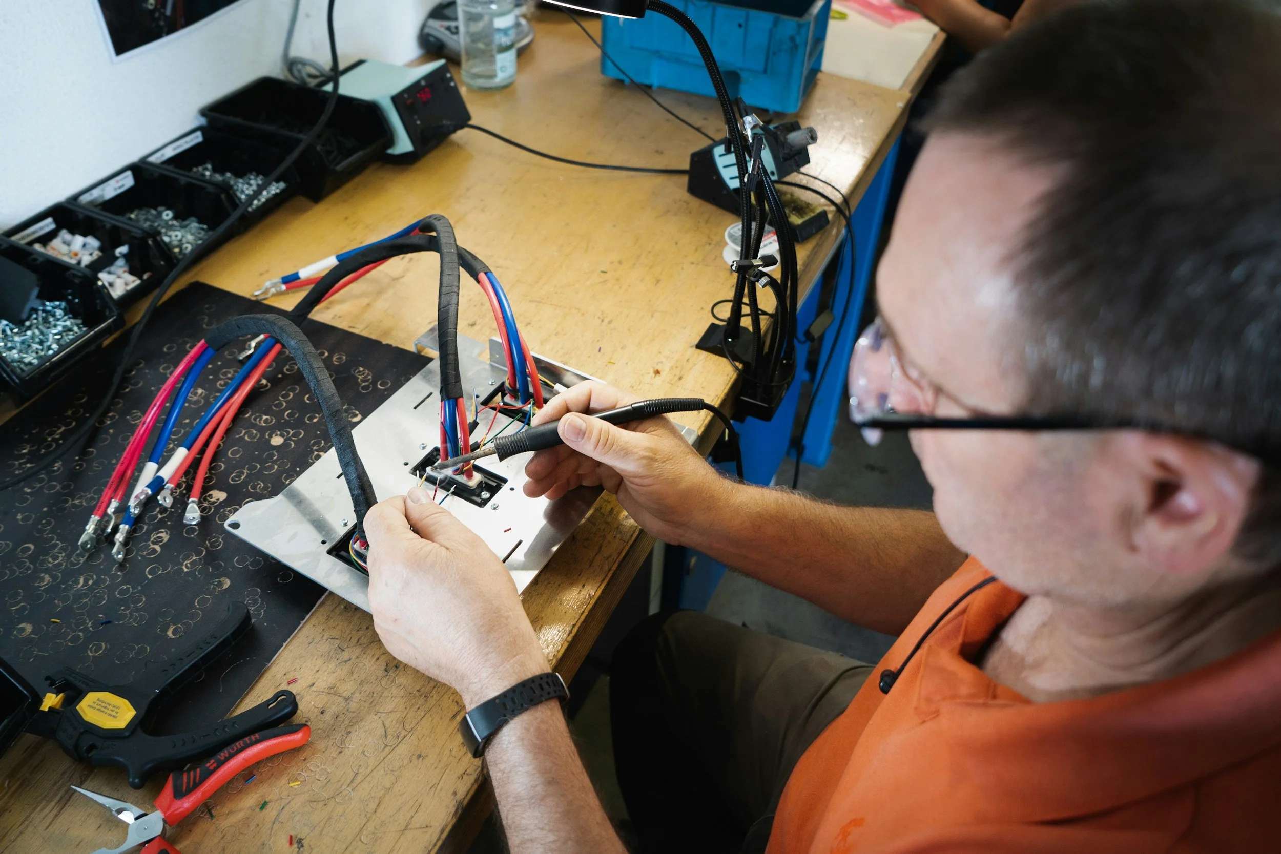 Person working on wiring and soldering electrical cables on a metal panel in a workshop.