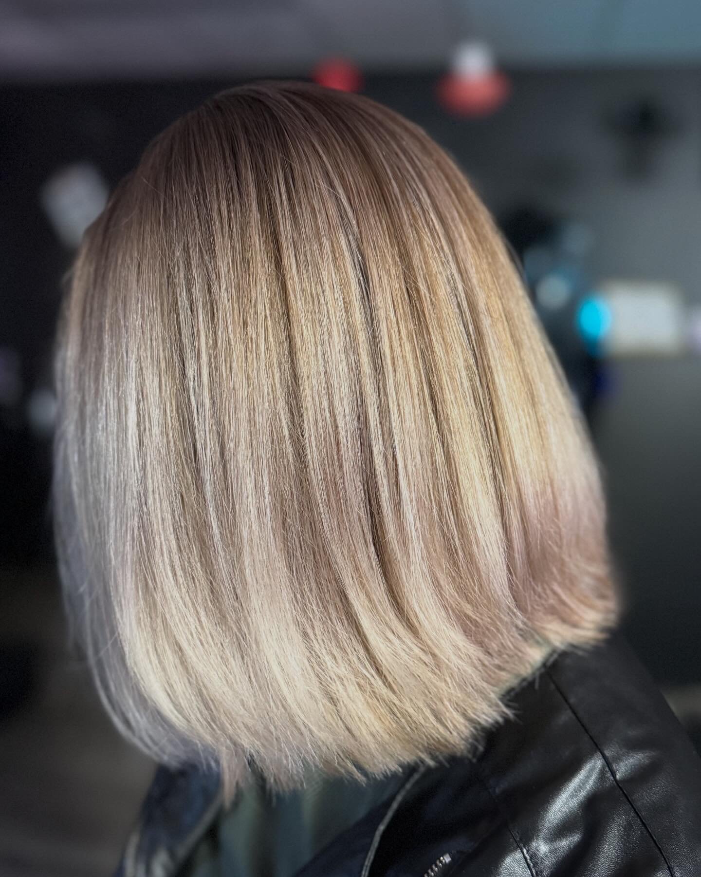 Close-up of a person's hair in a bob cut with blonde color and subtle pink tones, shot from the side with a dark background.