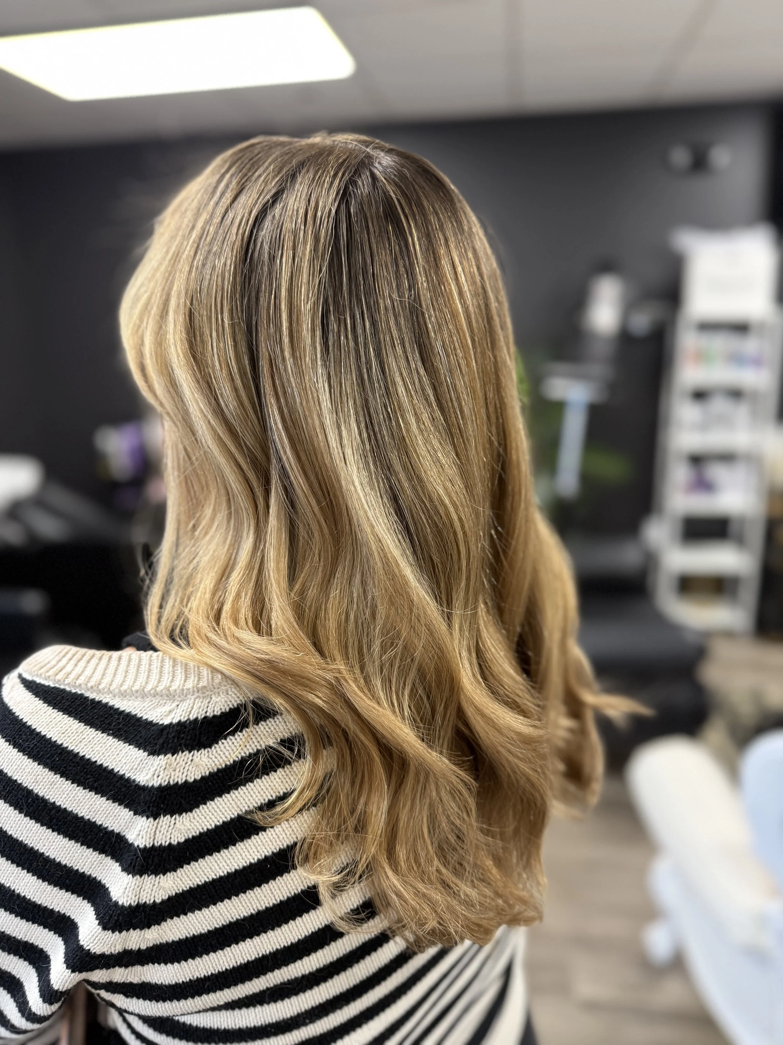 Person with shoulder-length wavy blonde hair wearing a black and white striped sweater in a salon.