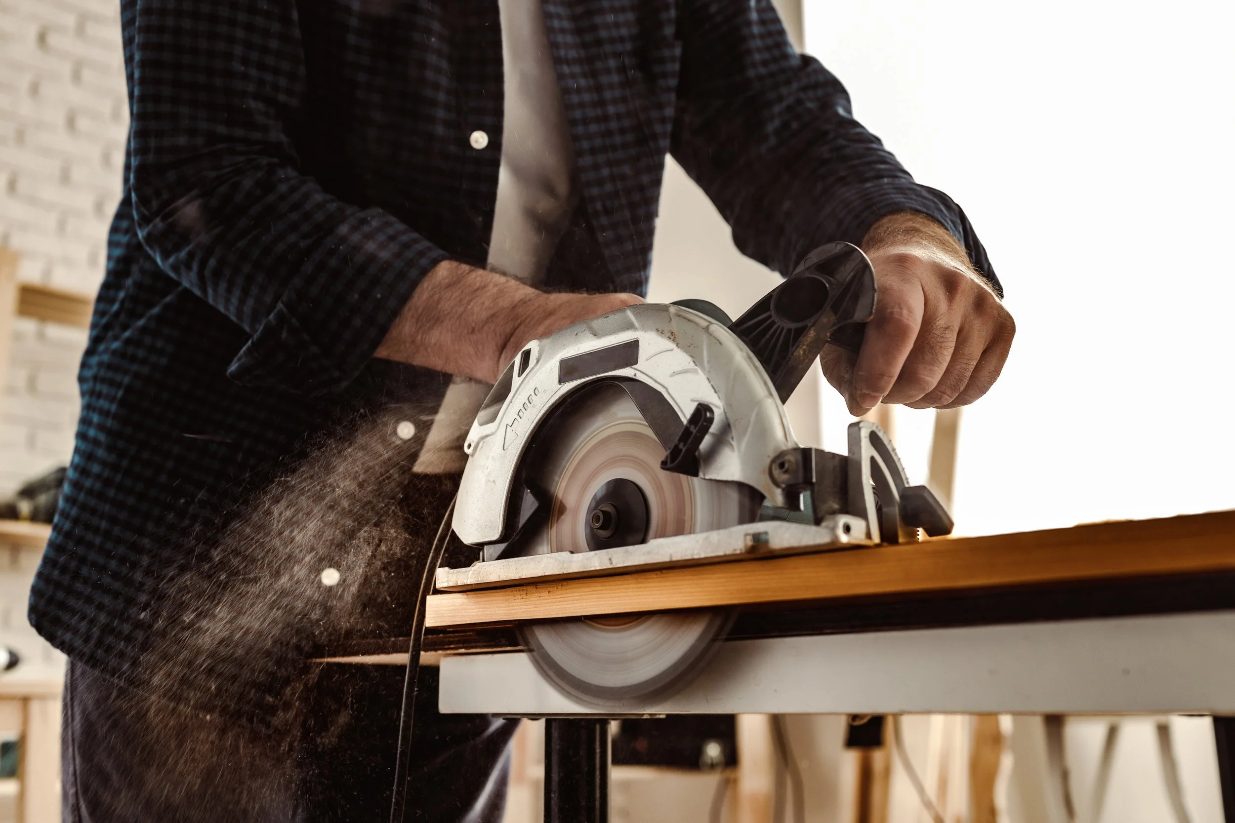 Person using a circular saw to cut a piece of wood in a woodworking shop.