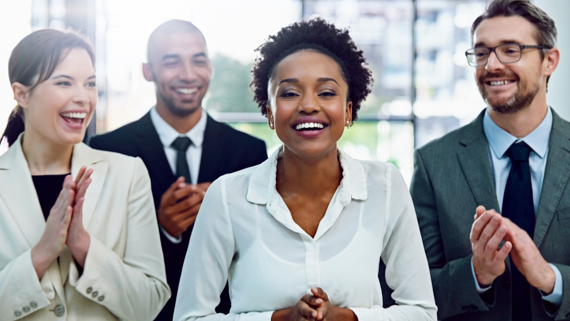 Group of four diverse business people smiling and clapping in a bright office.
