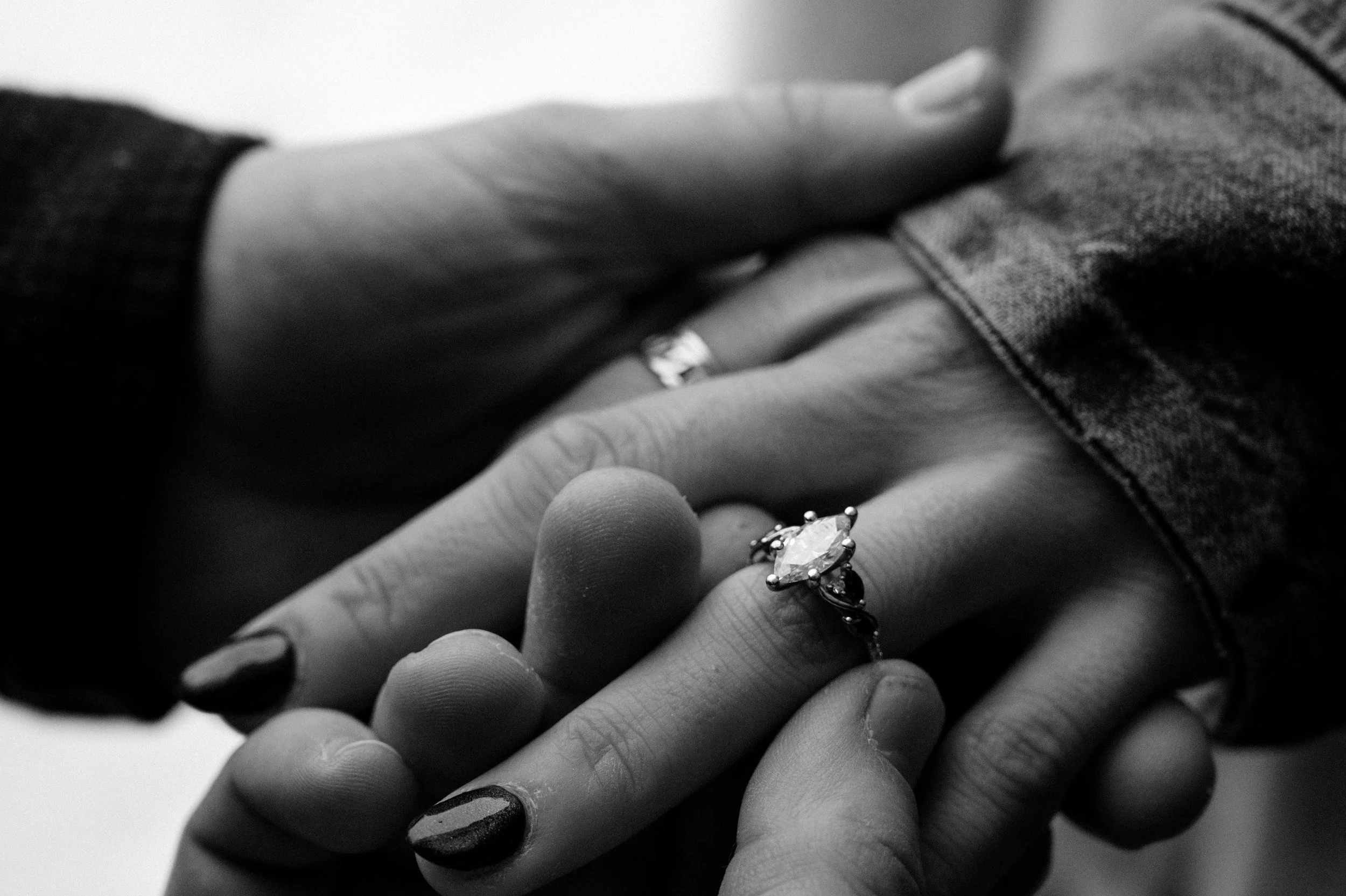 Close-up of two hands with rings, one hand with painted nails resting on top of the other, in black and white.