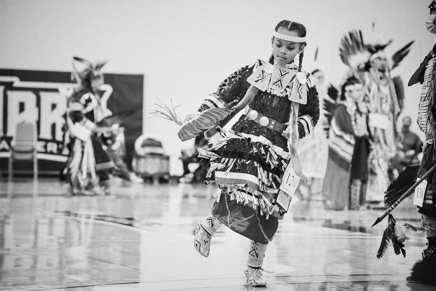Young girl in traditional Native American dress performing a dance at a cultural event.
