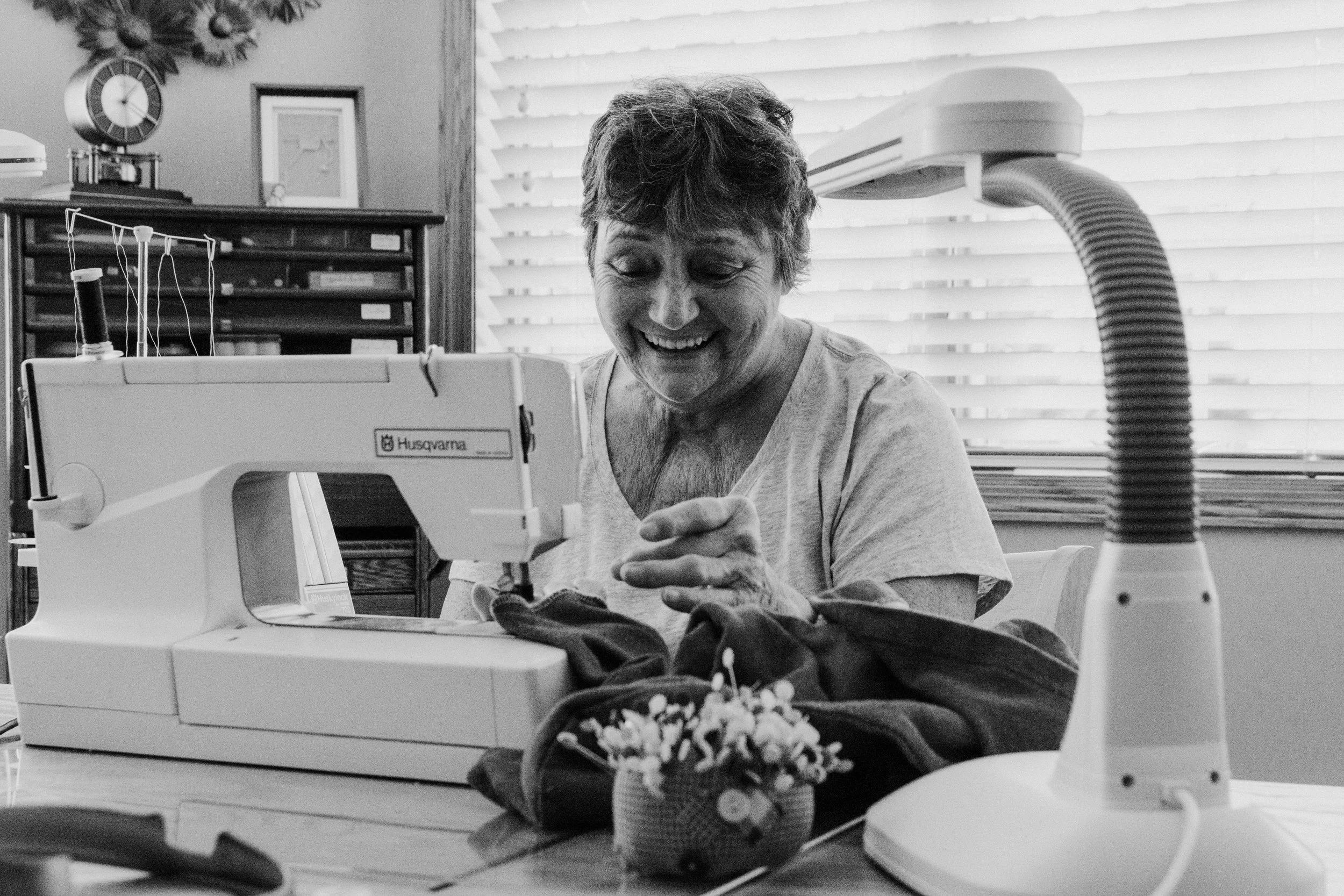 An elderly woman sewing on a sewing machine, smiling while working.