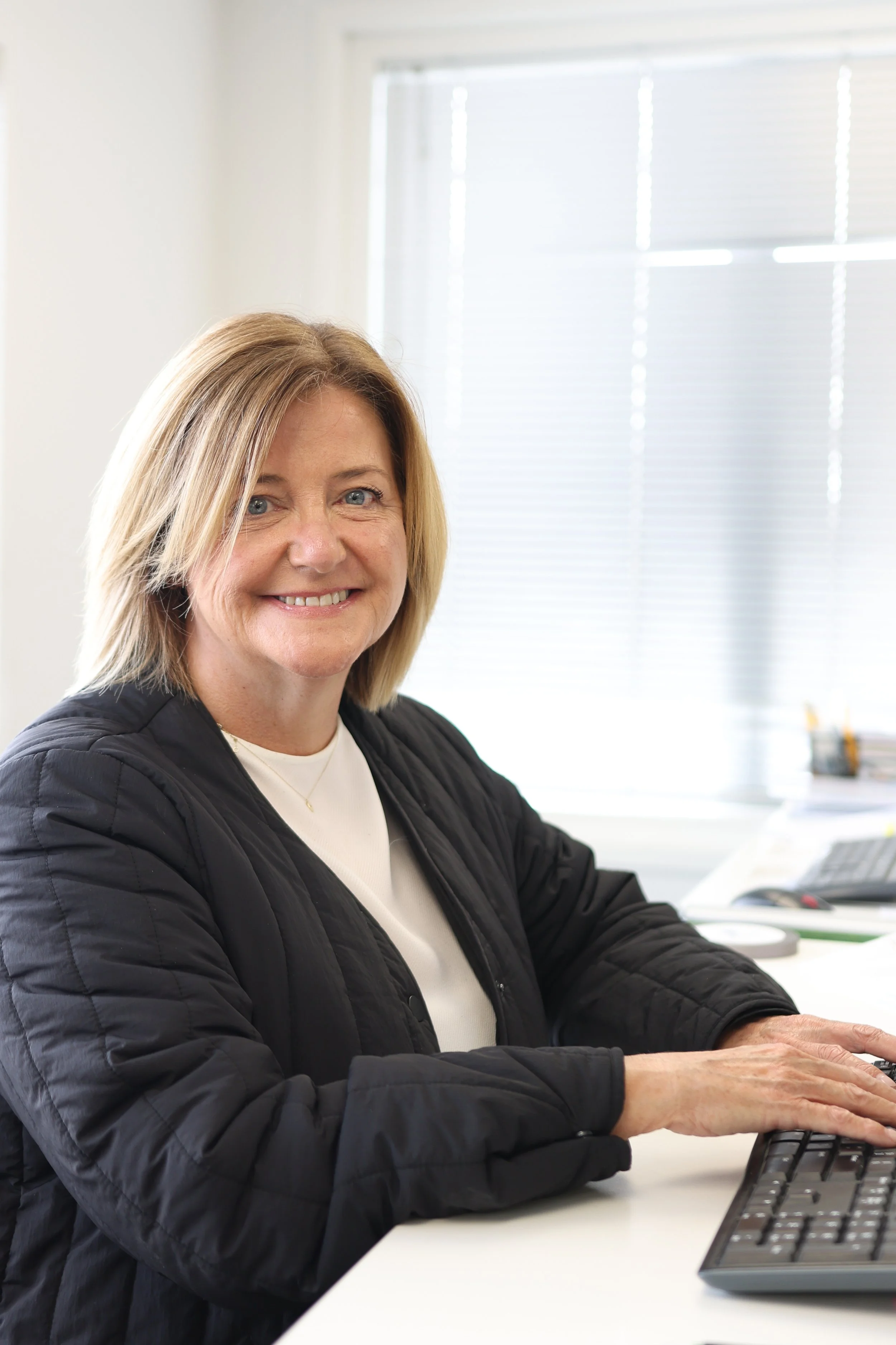 Smiling woman sitting at a desk and typing on a keyboard in an office setting.