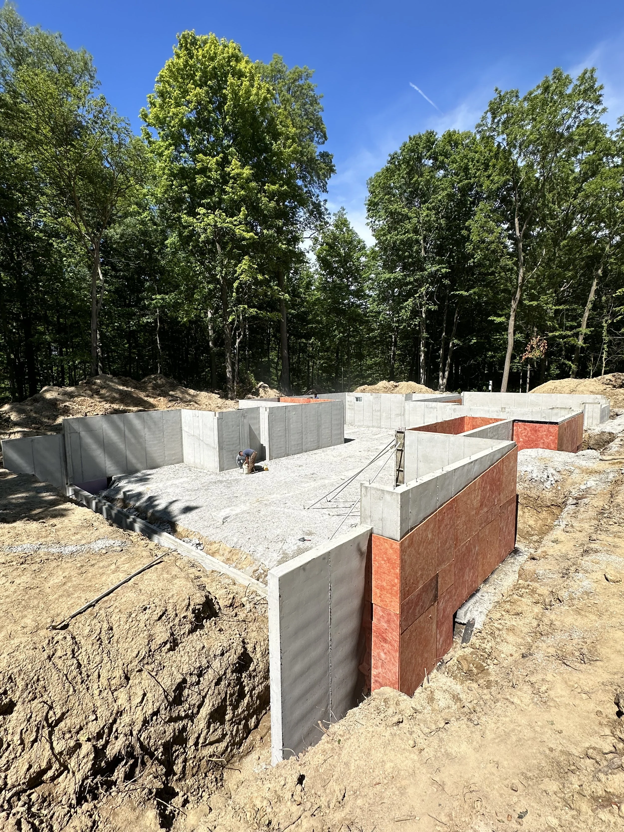 Construction site with concrete foundation walls in a forested area on a sunny day.