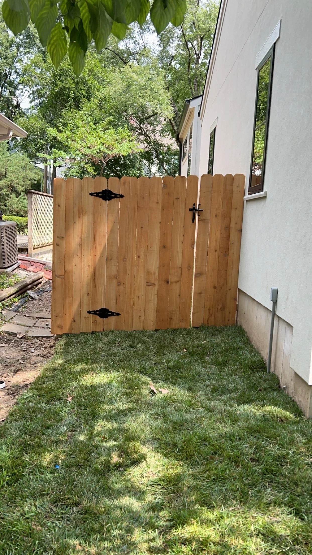 Wooden backyard gate attached to the side of a white house with green lawn and trees in the background.
