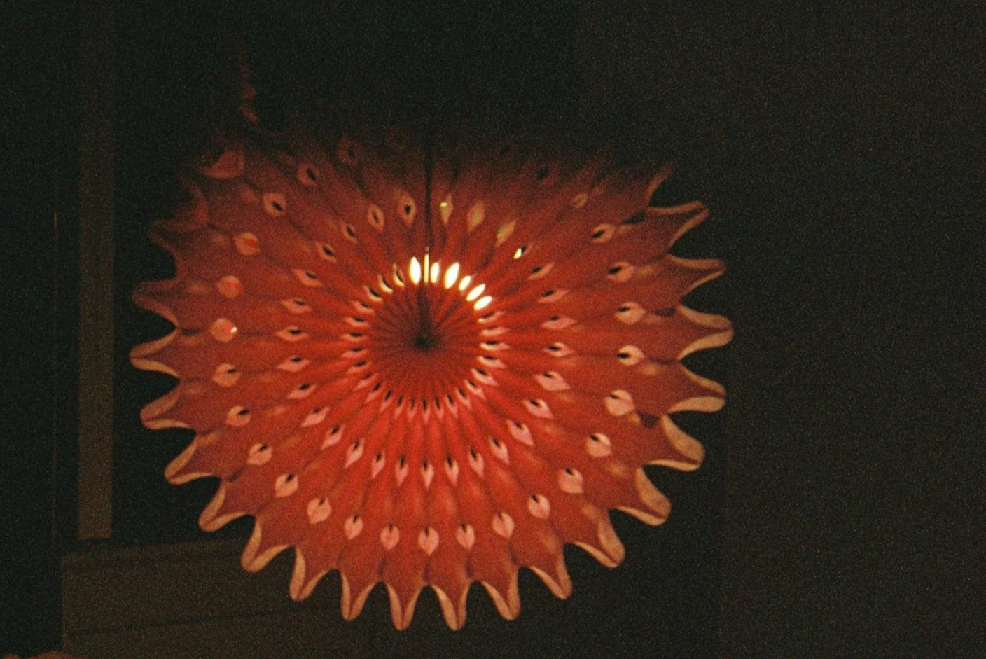Decorative orange paper lantern with a circular pattern, hanging in a dimly lit space.