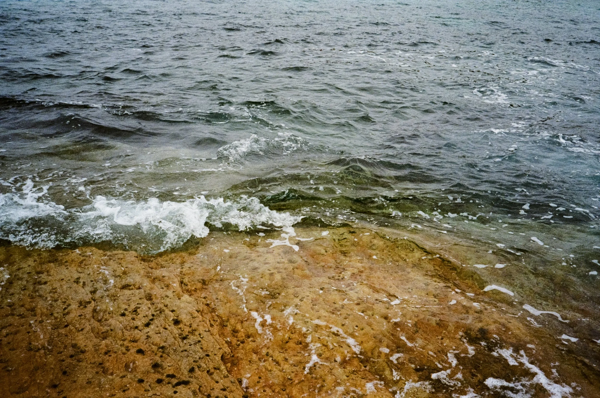 Close-up of a rocky shoreline with gentle waves and water lapping onto the rocks.