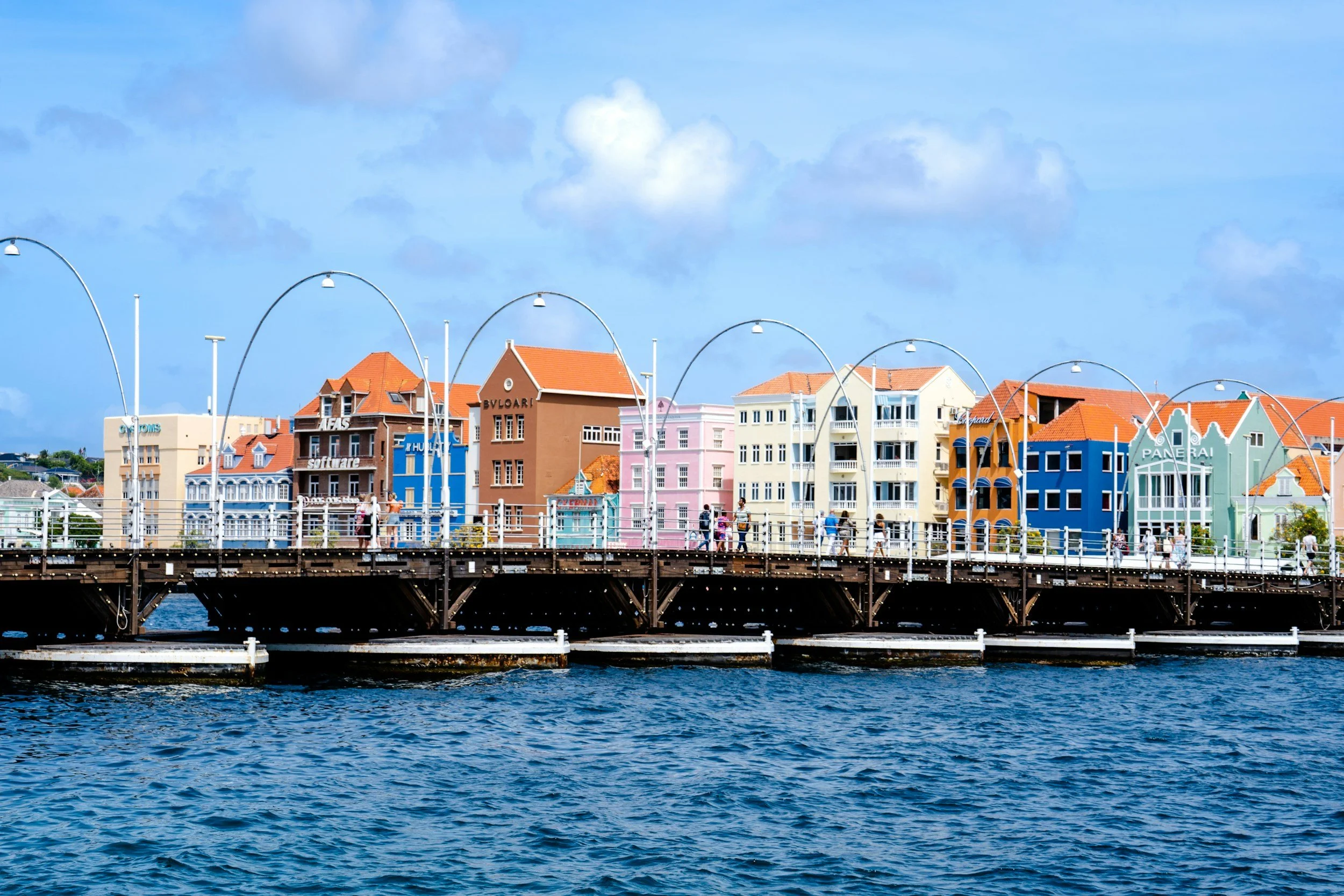 Colorful buildings with red roofs along a waterfront, viewed from a body of water.