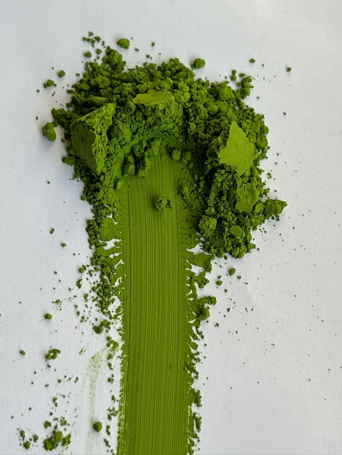 Close-up of bright green matcha powder with a streak of ground green tea leaves on white background.