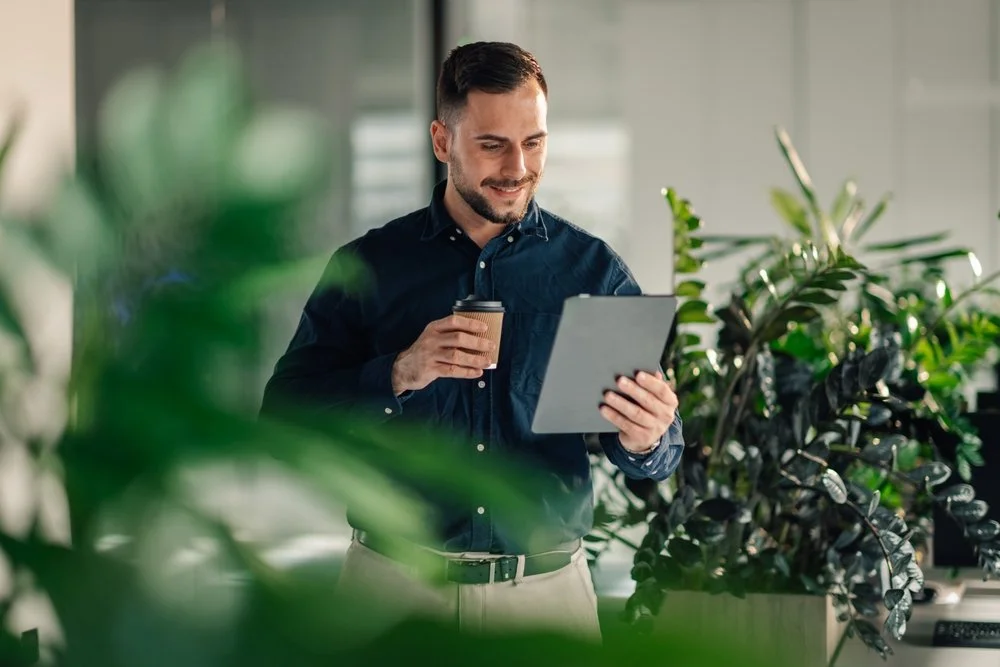 A business professional standing among office plants reviewing information on a tablet while managing IT support for his Langley company