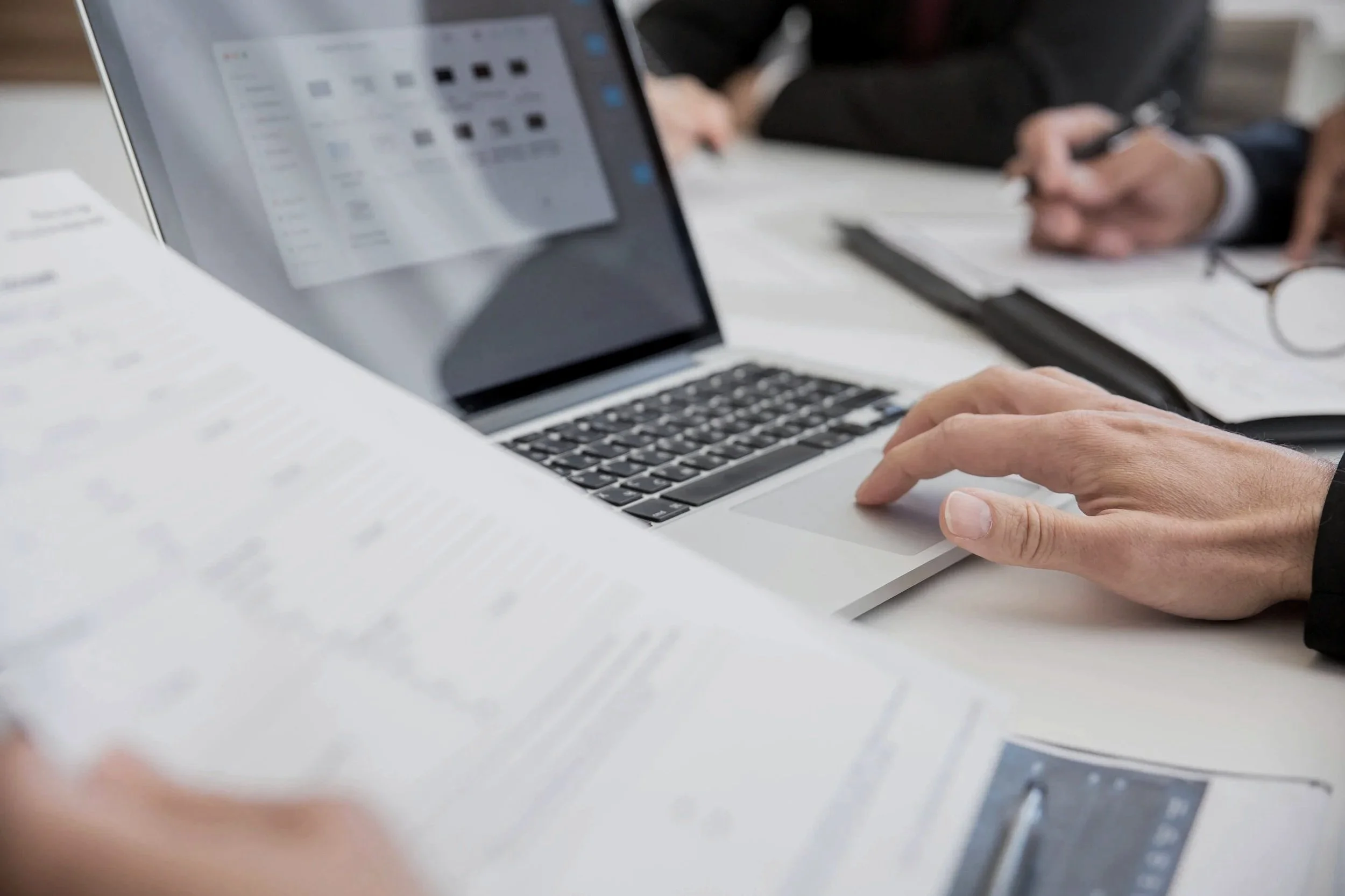 A professional reviewing printed documents while working on a laptop at a desk, working on network security solutions and an assessement for a Vancouver businesses