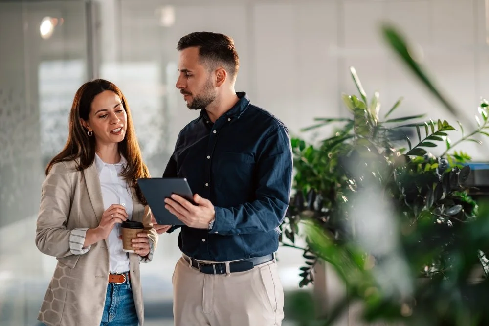 A man and woman standing in a bright office space looking at a tablet together while evaluating IT support options for their Langley business