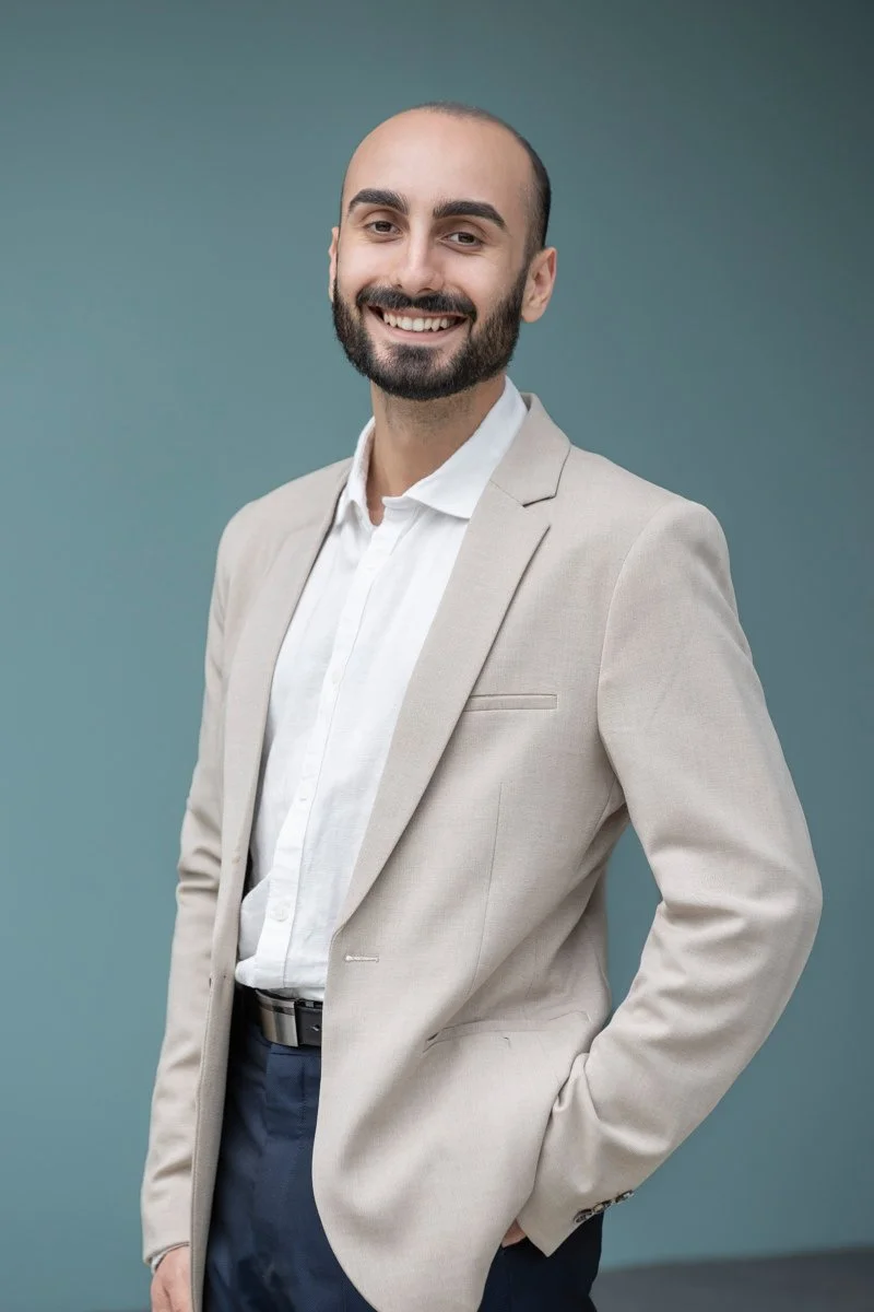 Portrait of Federico Moreno smiling confidently, wearing a light blazer and white shirt against a soft blue background.