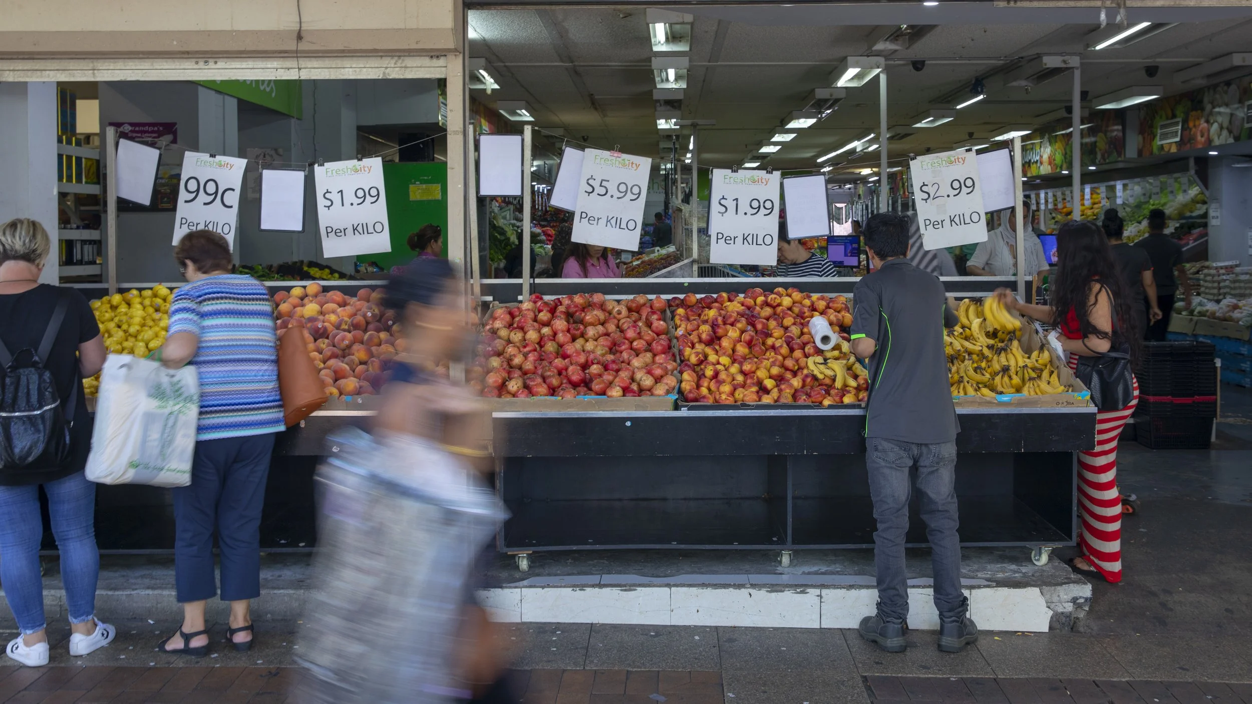 Fruit and vegetable shop with fresh produce n the street with people walking by.