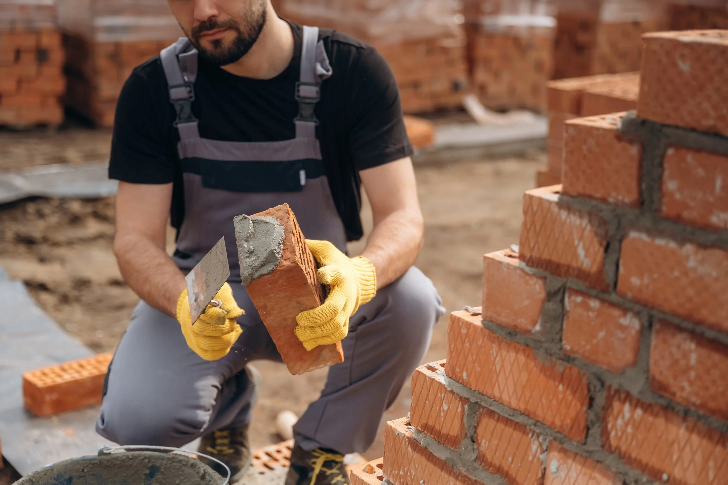 Person applying cement to a brick they will lay on a wall foundation.