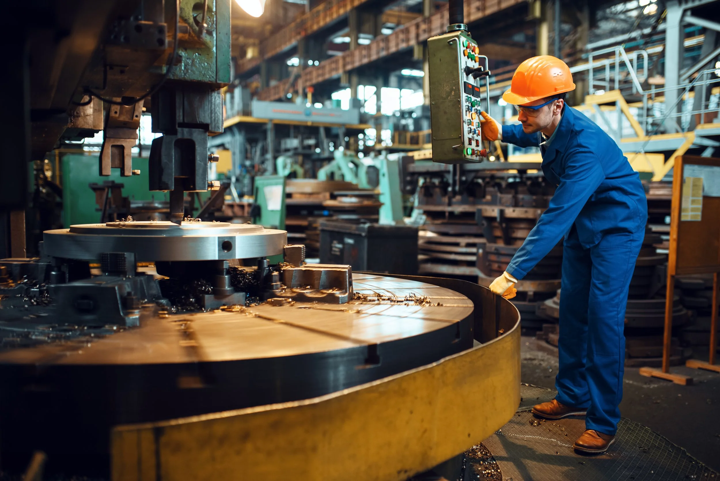 Worker operating a large metal lathe in a manufacturing factory