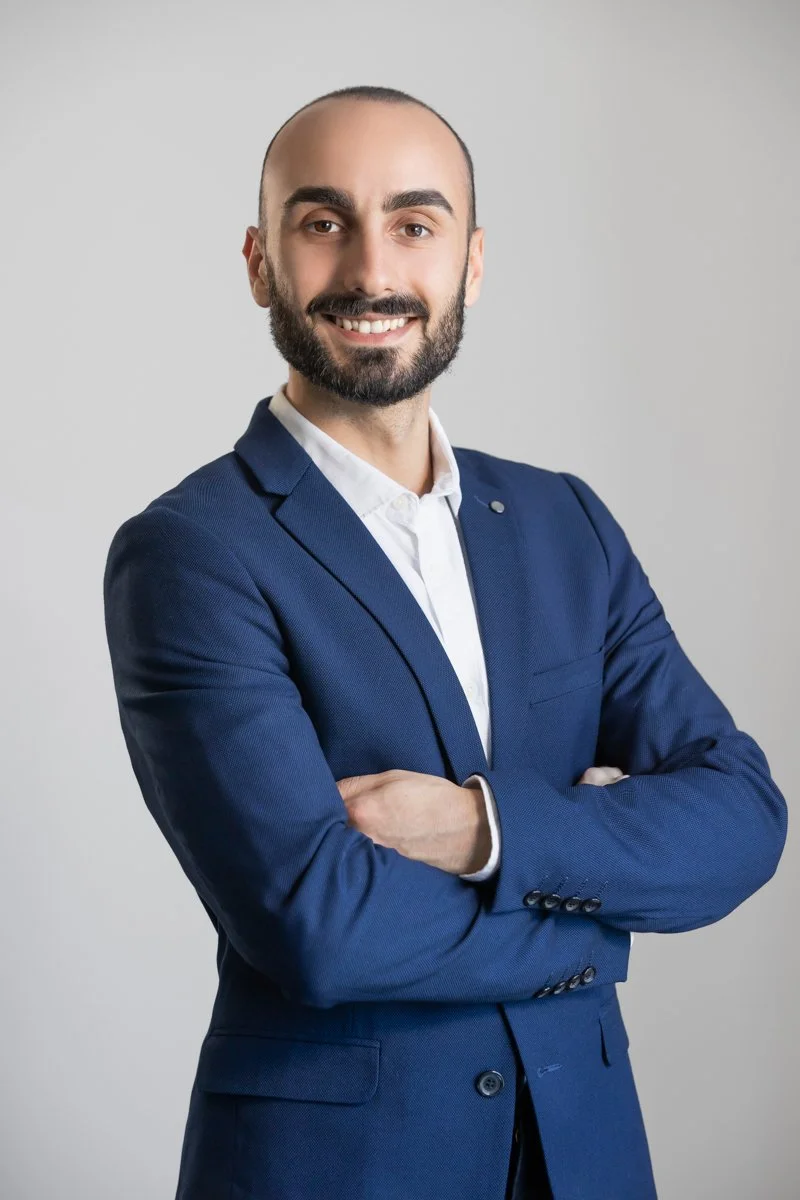Portrait of Federico Moreno smiling with arms crossed, wearing a blue suit jacket and white shirt against a light neutral background.