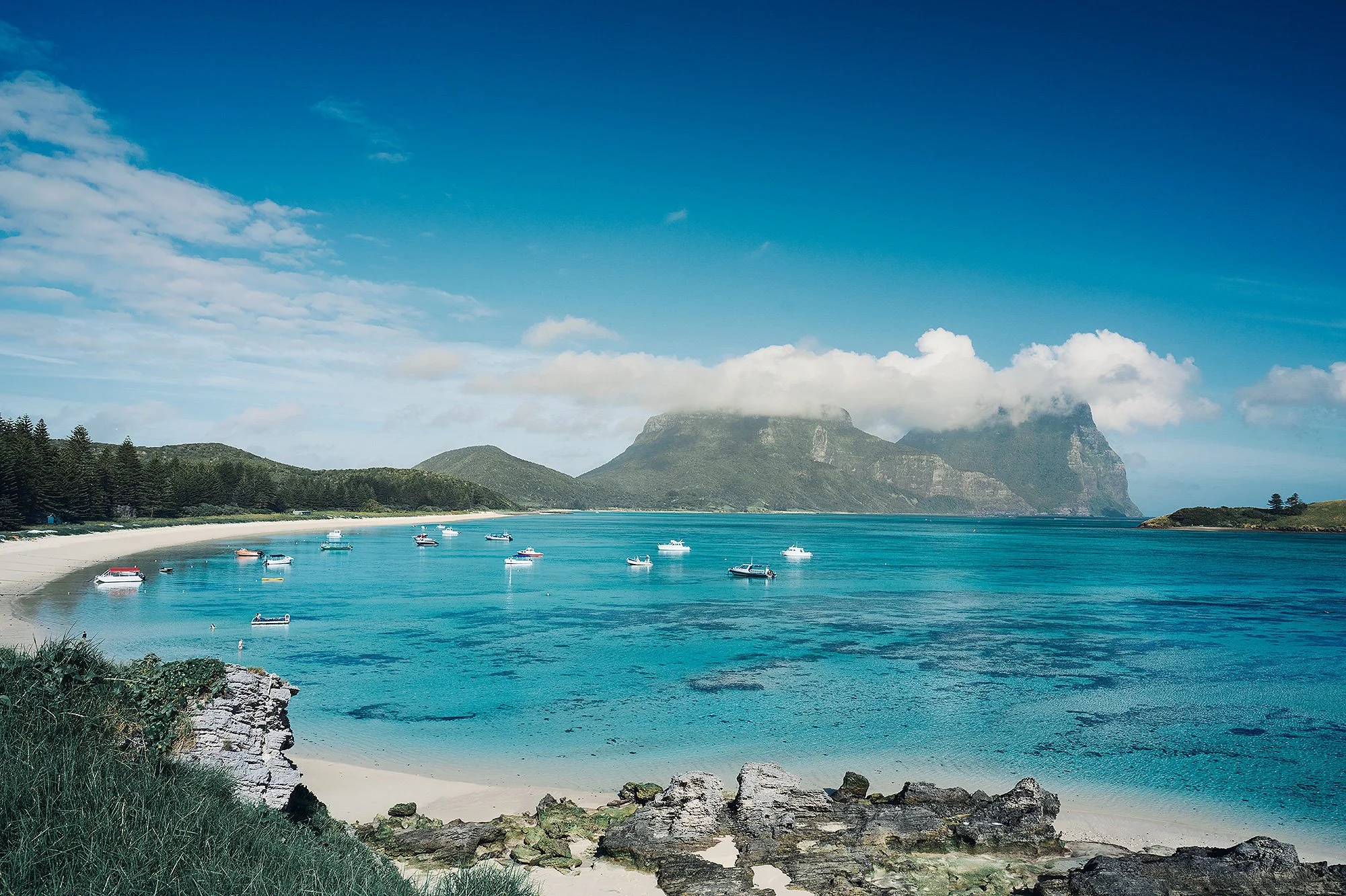 Blue bay with boats anchored and green mountains in the background